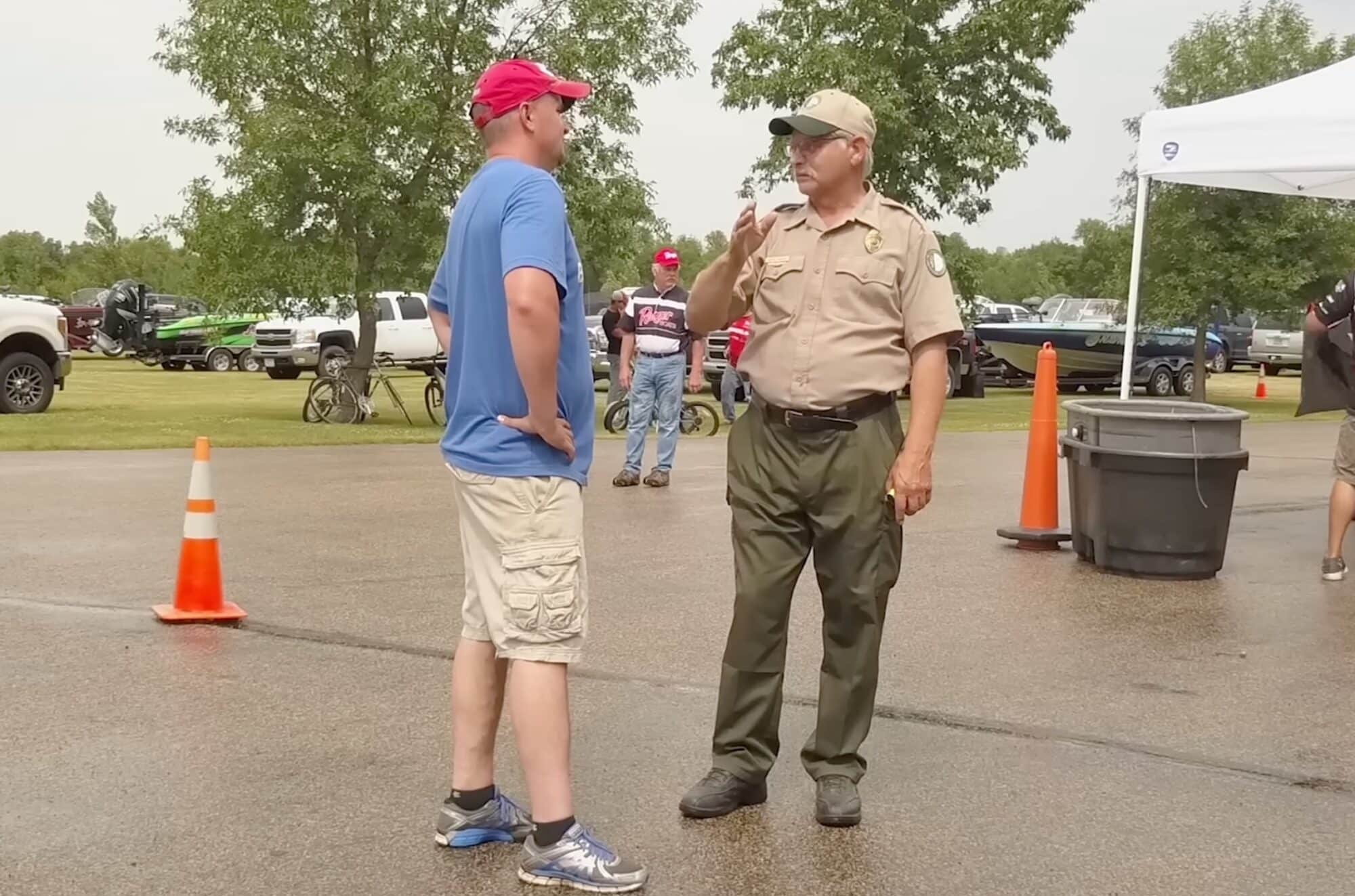 A drone pilot in a red cap speaking with a uniformed park ranger outdoors.