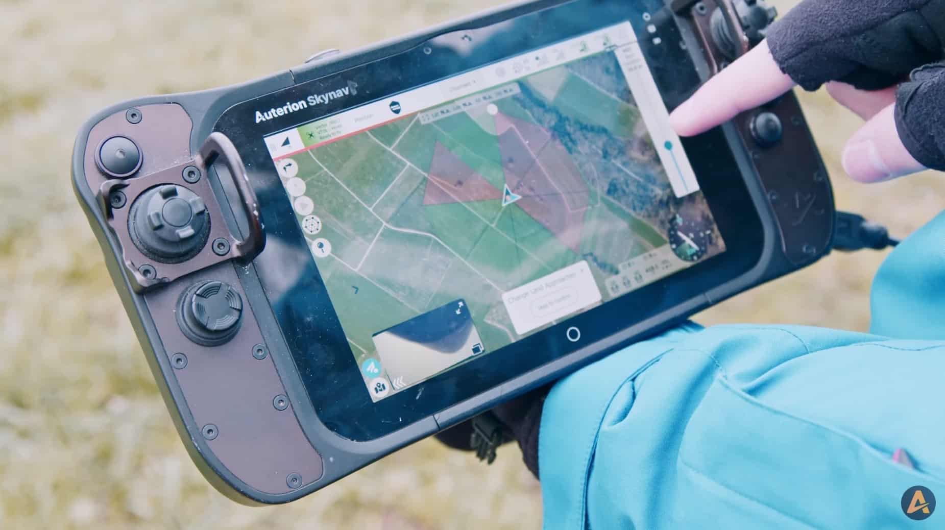 Gloved operator holds an Auterion Skynav ground controller showing a live mission map.