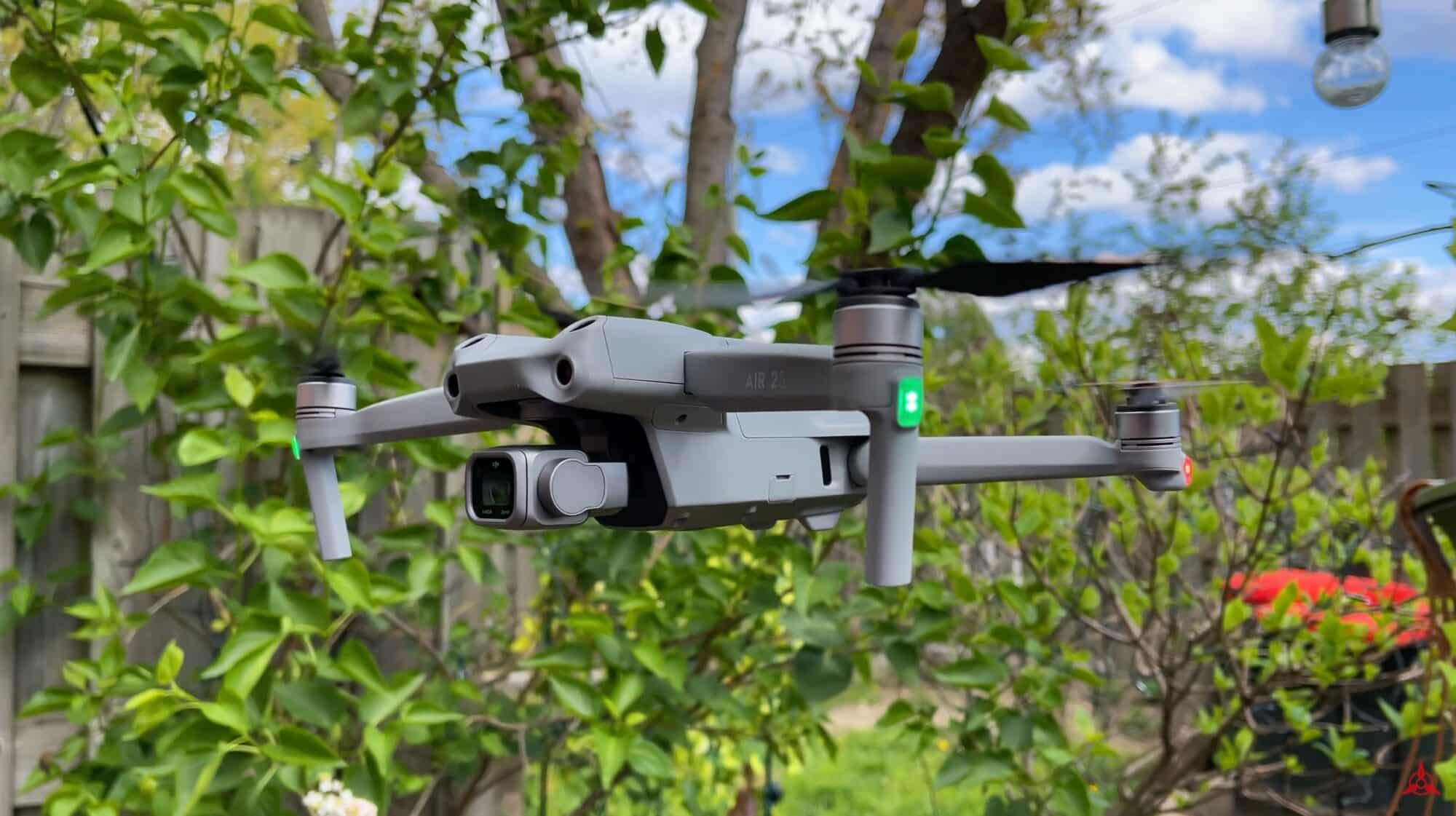 DJI Air 2S hovering among green branches in a suburban backyard.