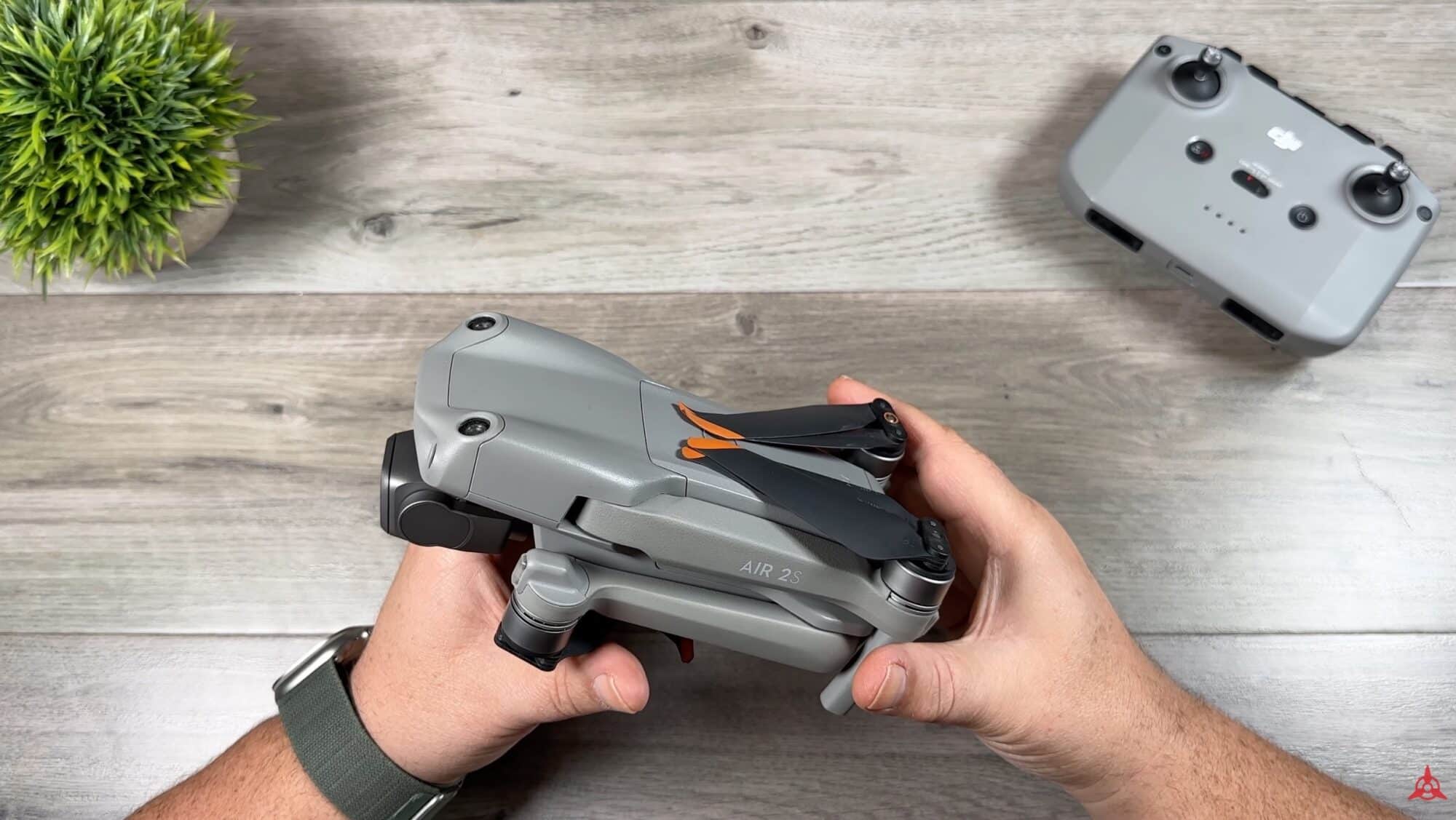 Hands hold a folded DJI Air 2S beside its controller on a wooden table.