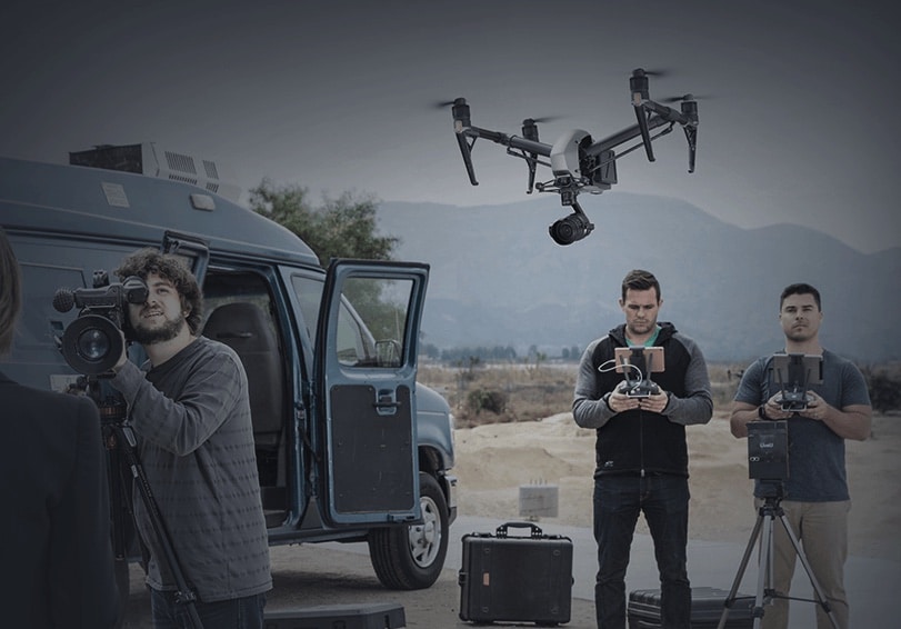 DJI Inspire 2 hovers above a film crew operating cameras and controllers outdoors.