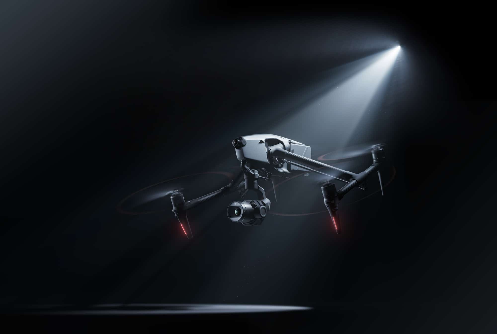 Professional cinema drone hovering in darkness beneath a single narrow spotlight.