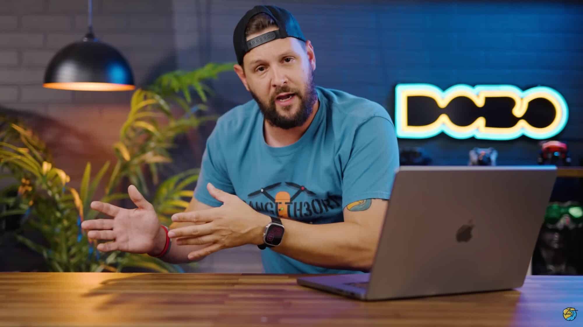 Video host discussing Chinese drone bans from a studio desk with a laptop.