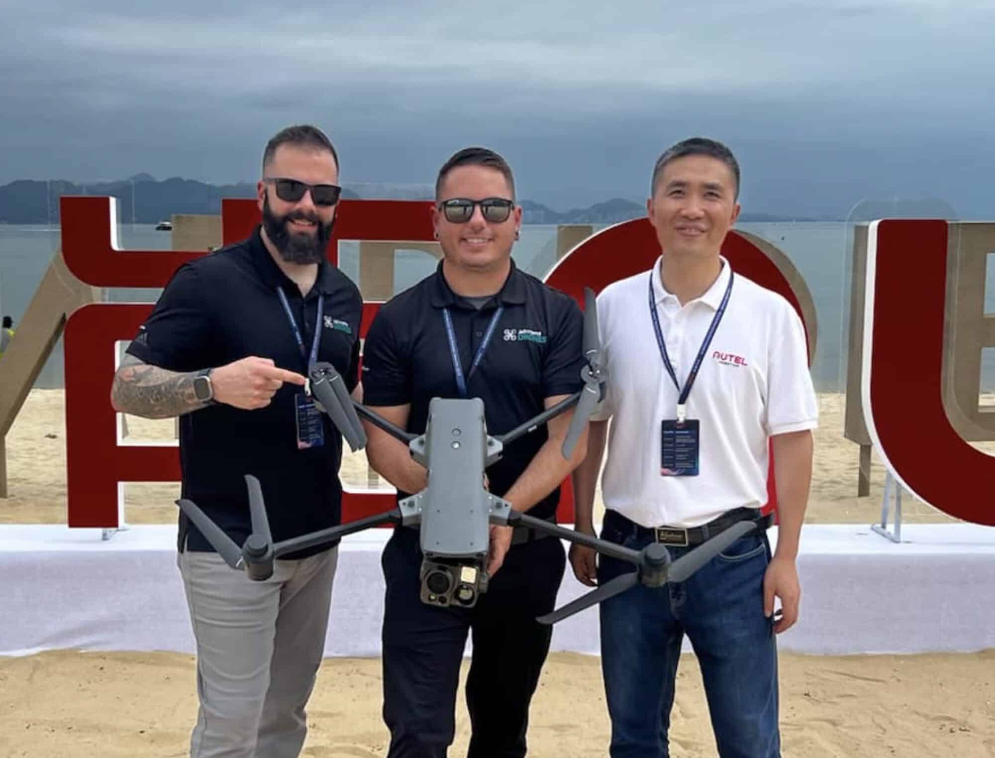 Three Autel representatives hold a large orange enterprise drone at an outdoor launch event.