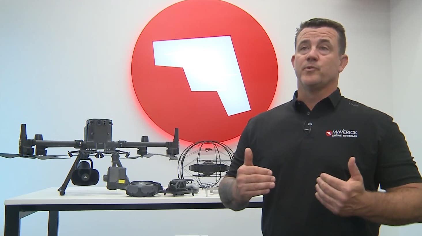 Presenter beside a table of enterprise drones in front of a red Maverick logo.