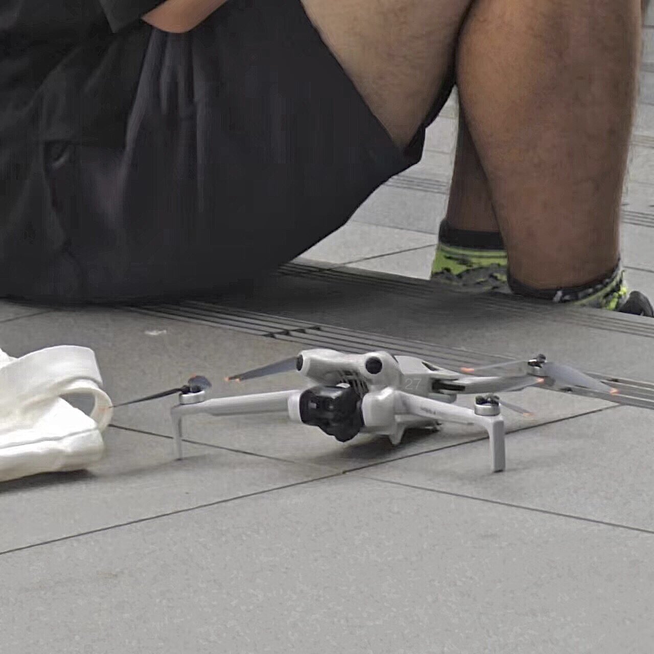 Leaked photo of a small white DJI drone on pavement beside a seated tester.