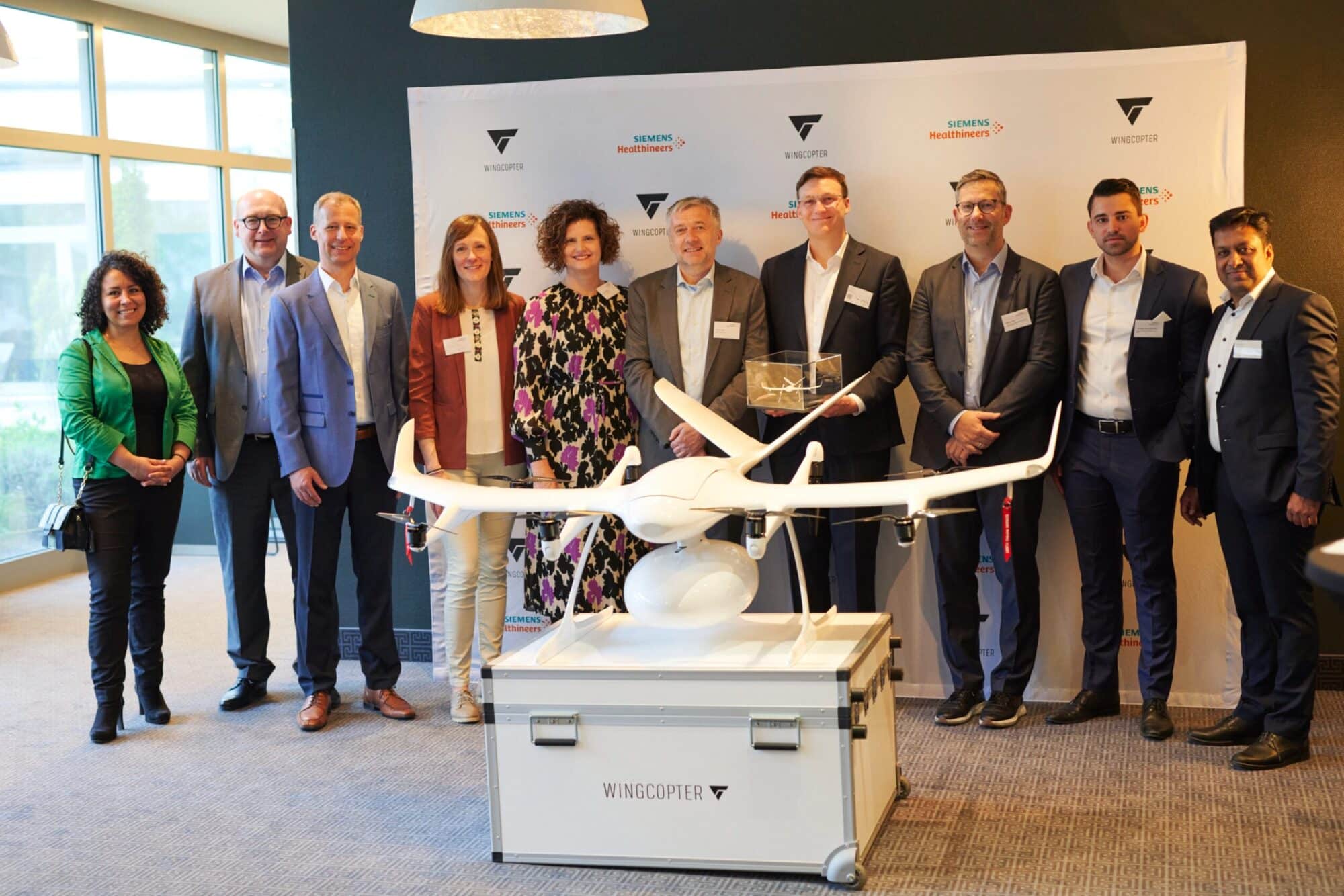Executives posing with a Wingcopter aircraft mounted on its transport case at a launch.
