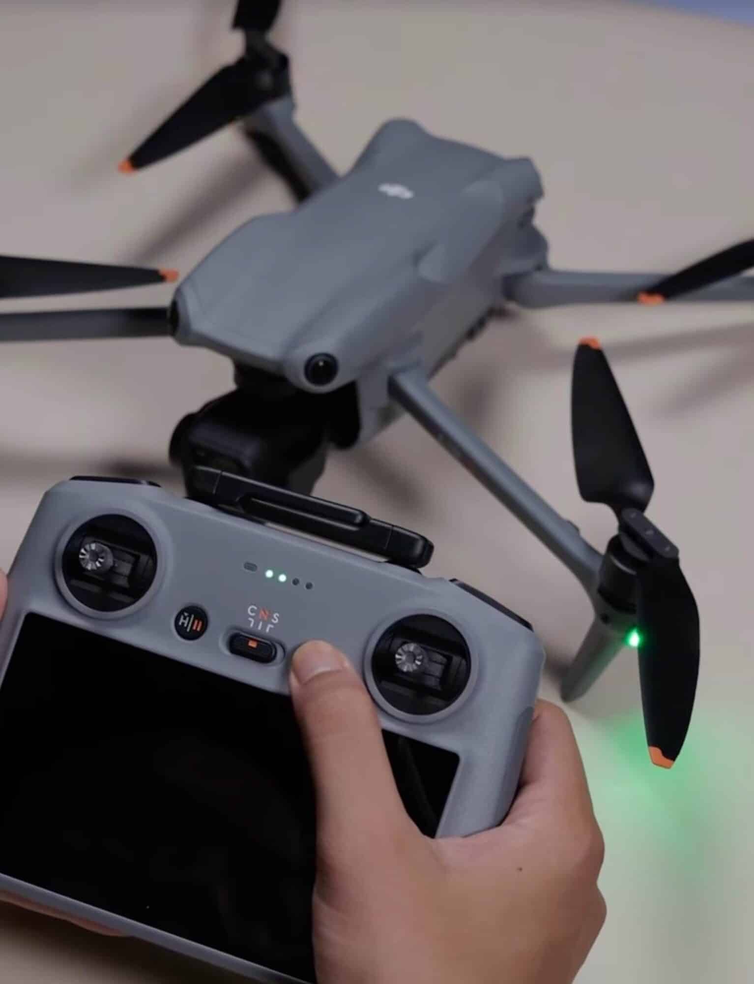 A thumb presses the controller power button as the Air 3 sits on a tripod.