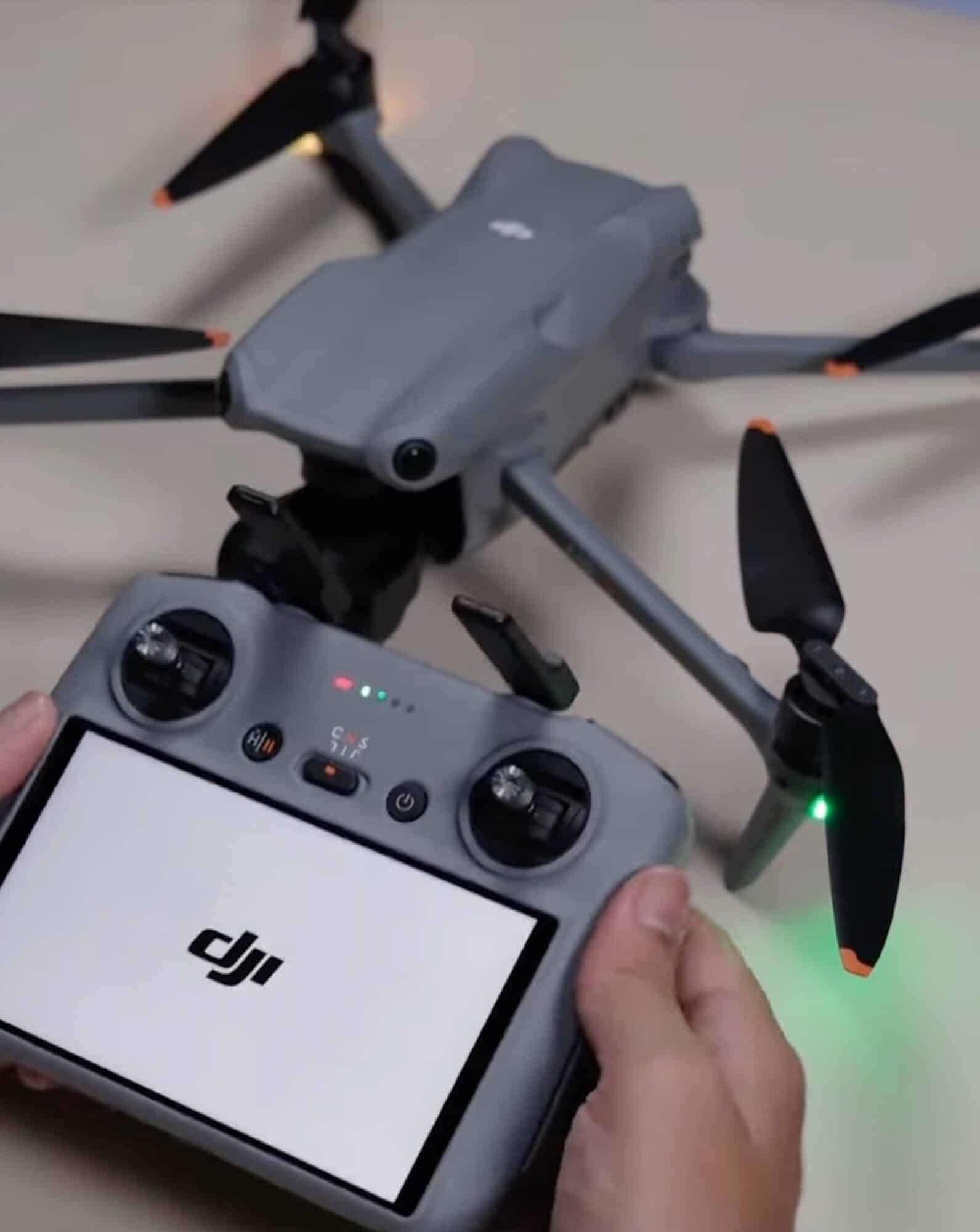 Hands hold a DJI RC controller showing the DJI logo beside the unfolded Air 3.