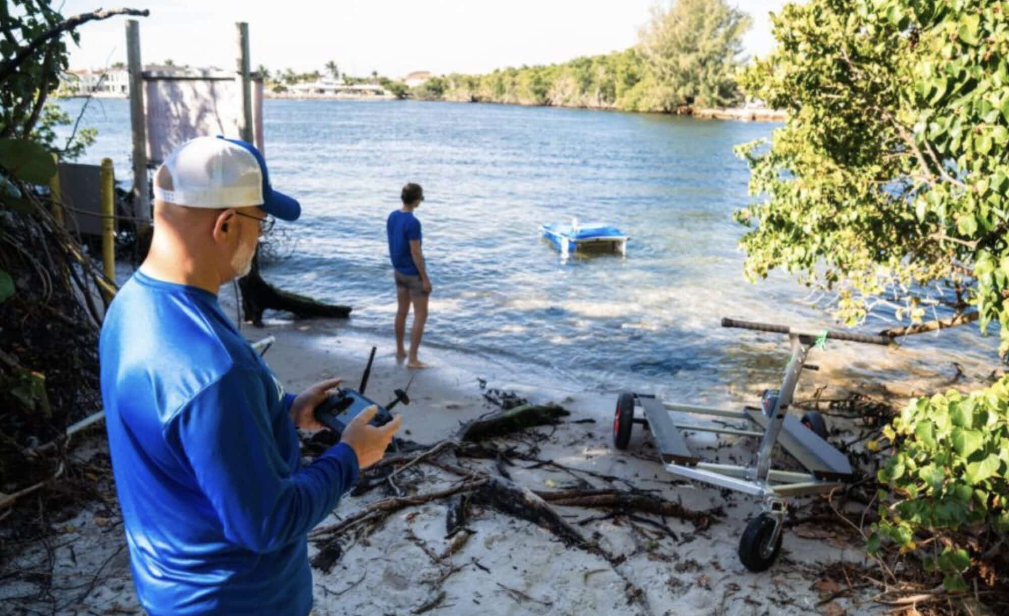 Operator on a shoreline steering the Pixie cleaning drone across a waterway.