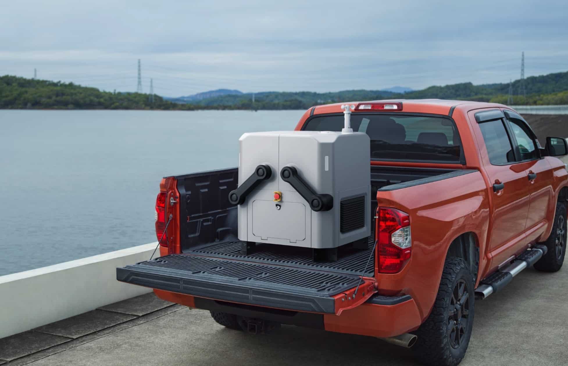 DJI Dock loaded in the bed of an orange pickup truck beside a lake.