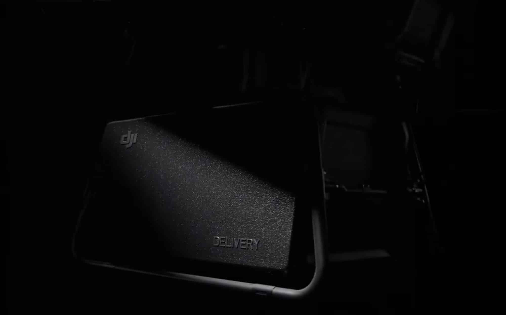Dim photo of a black DJI cargo container mounted beneath a delivery drone.