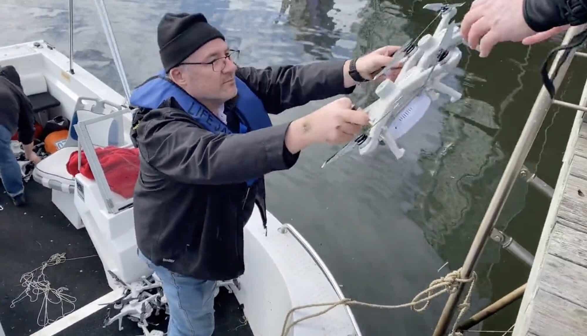 A man on a boat lifts a recovered light-show drone out of the water.