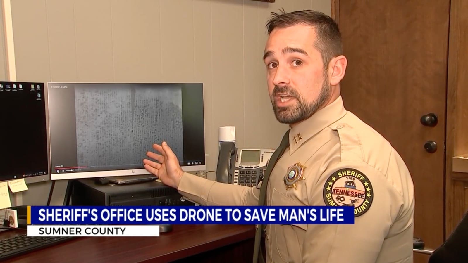 Sumner County deputy points at drone footage on a monitor during a news interview.