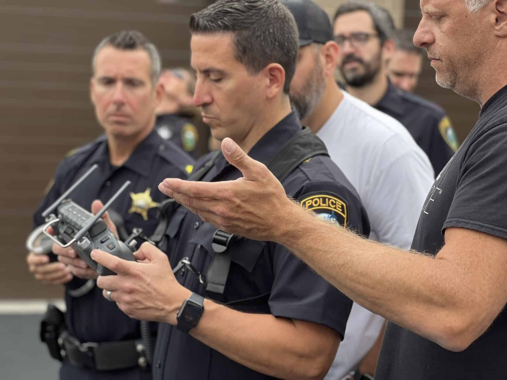 Police officers gather as one holds a DJI remote controller during outdoor training.