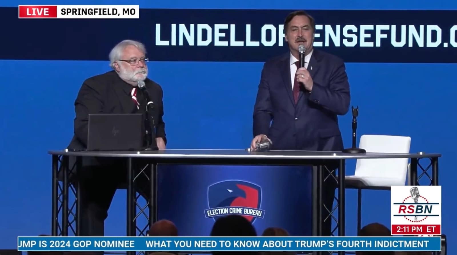 Live broadcast of two men presenting on stage under a Lindell fund banner.