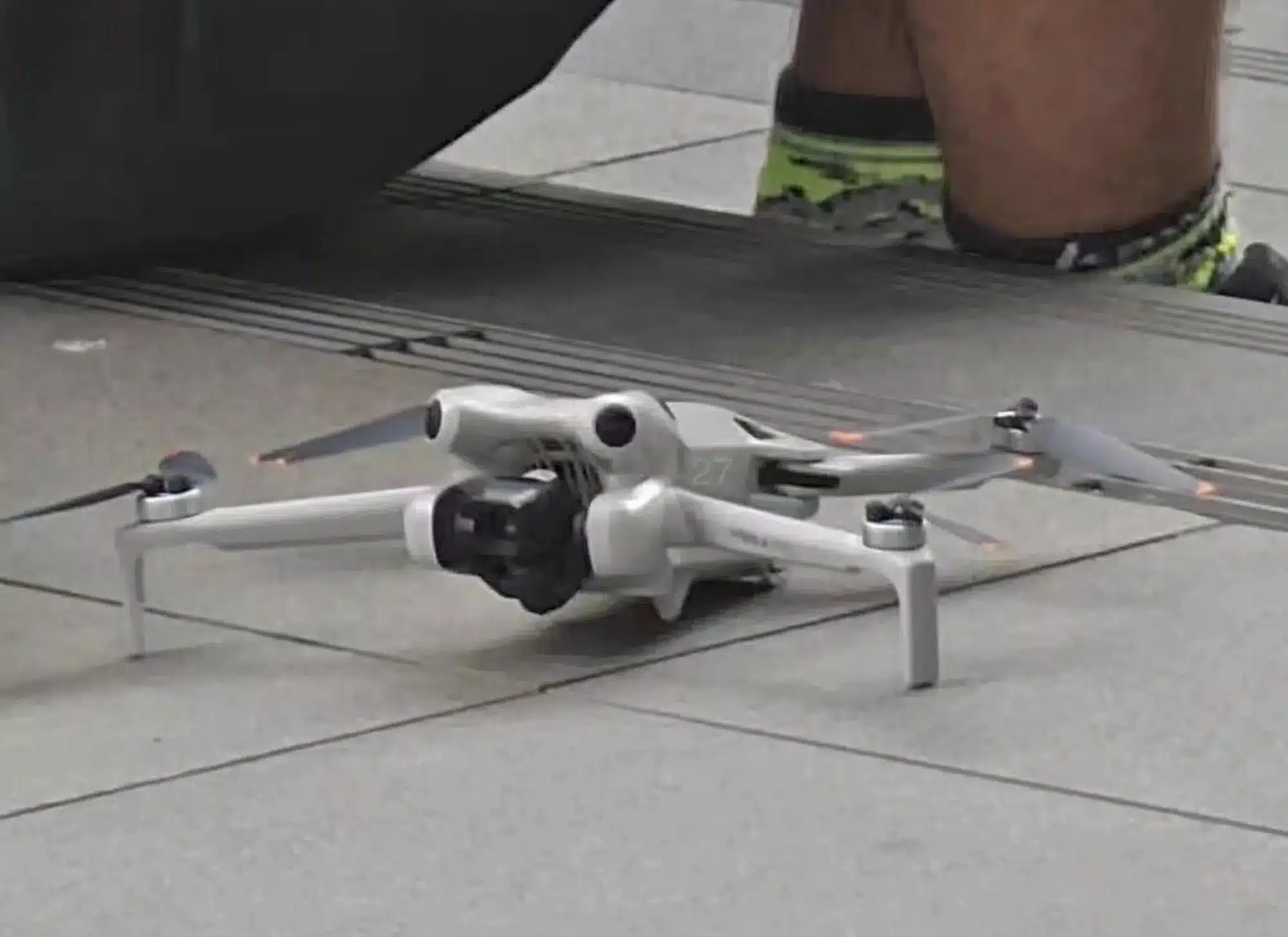 DJI Mini 4 Pro standing on a paving-stone floor with someone behind it.