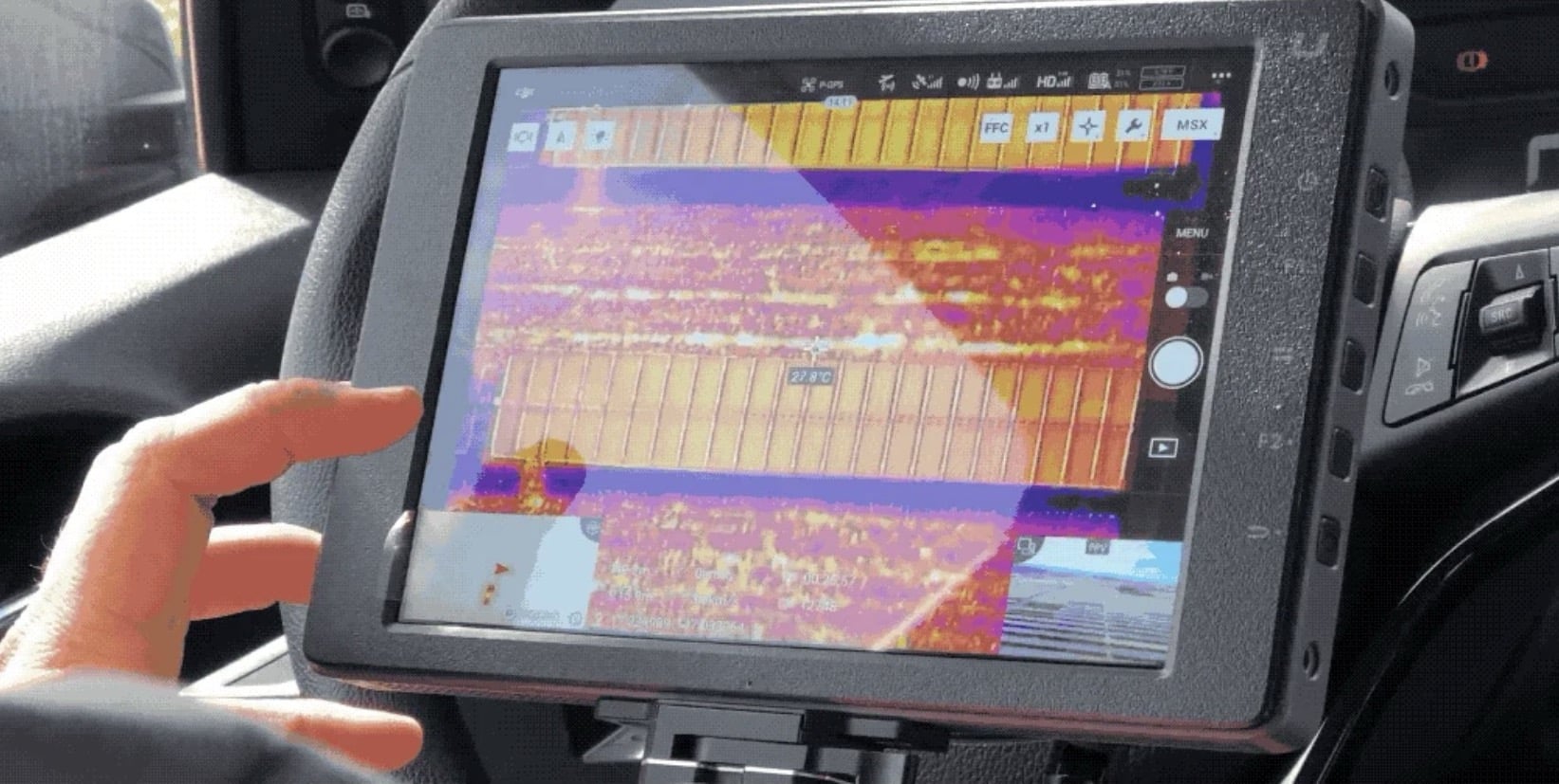 Hand on a rugged tablet showing a thermal map of solar panel rows.