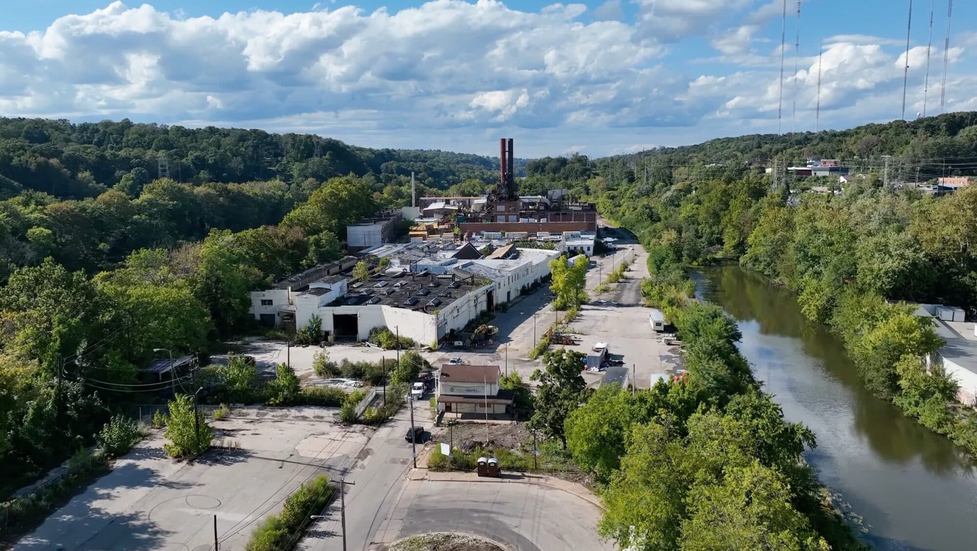 Aerial view of a derelict factory complex beside a river and woodland.