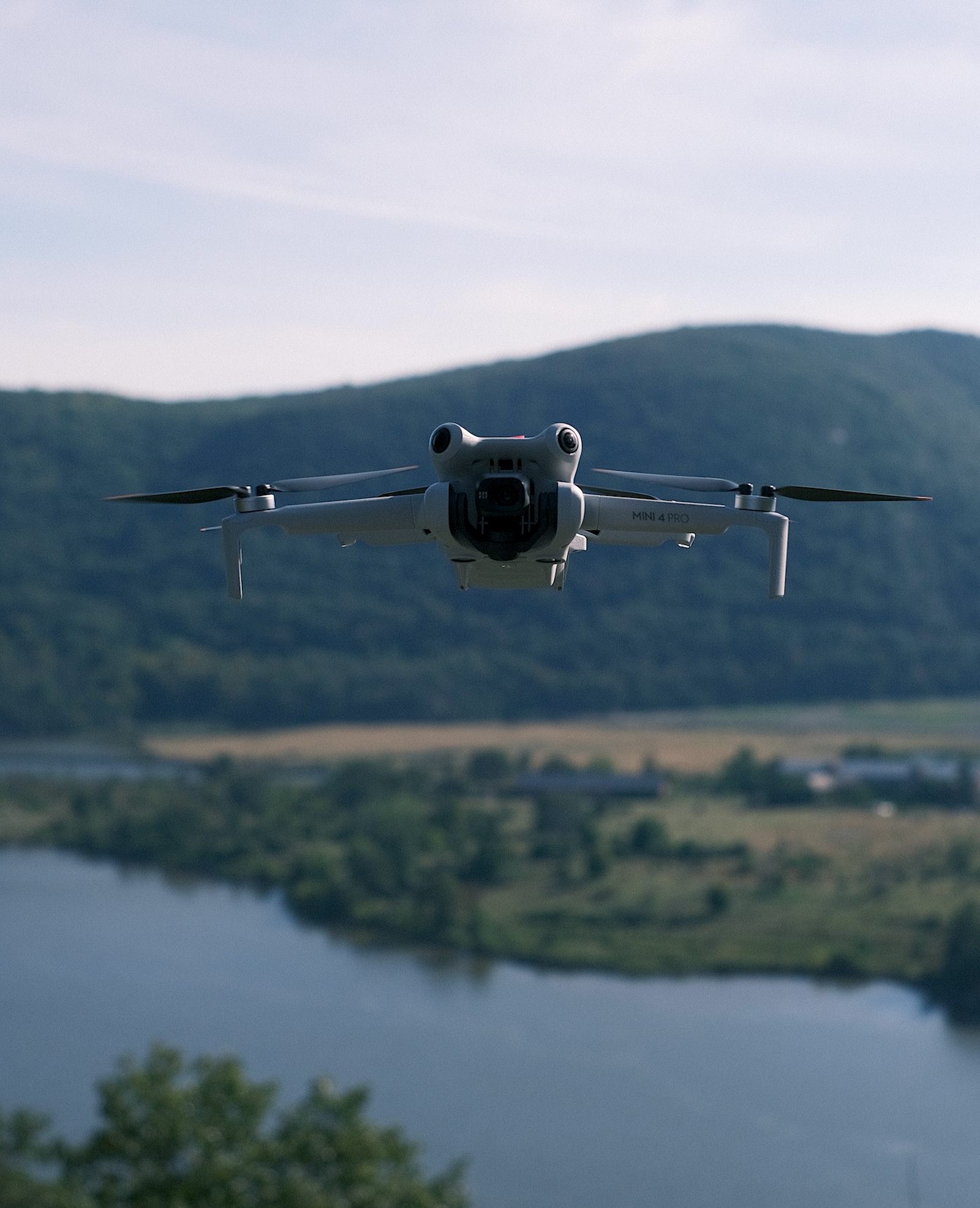 DJI Mini 4 Pro hovering above a wide river valley and green hills.