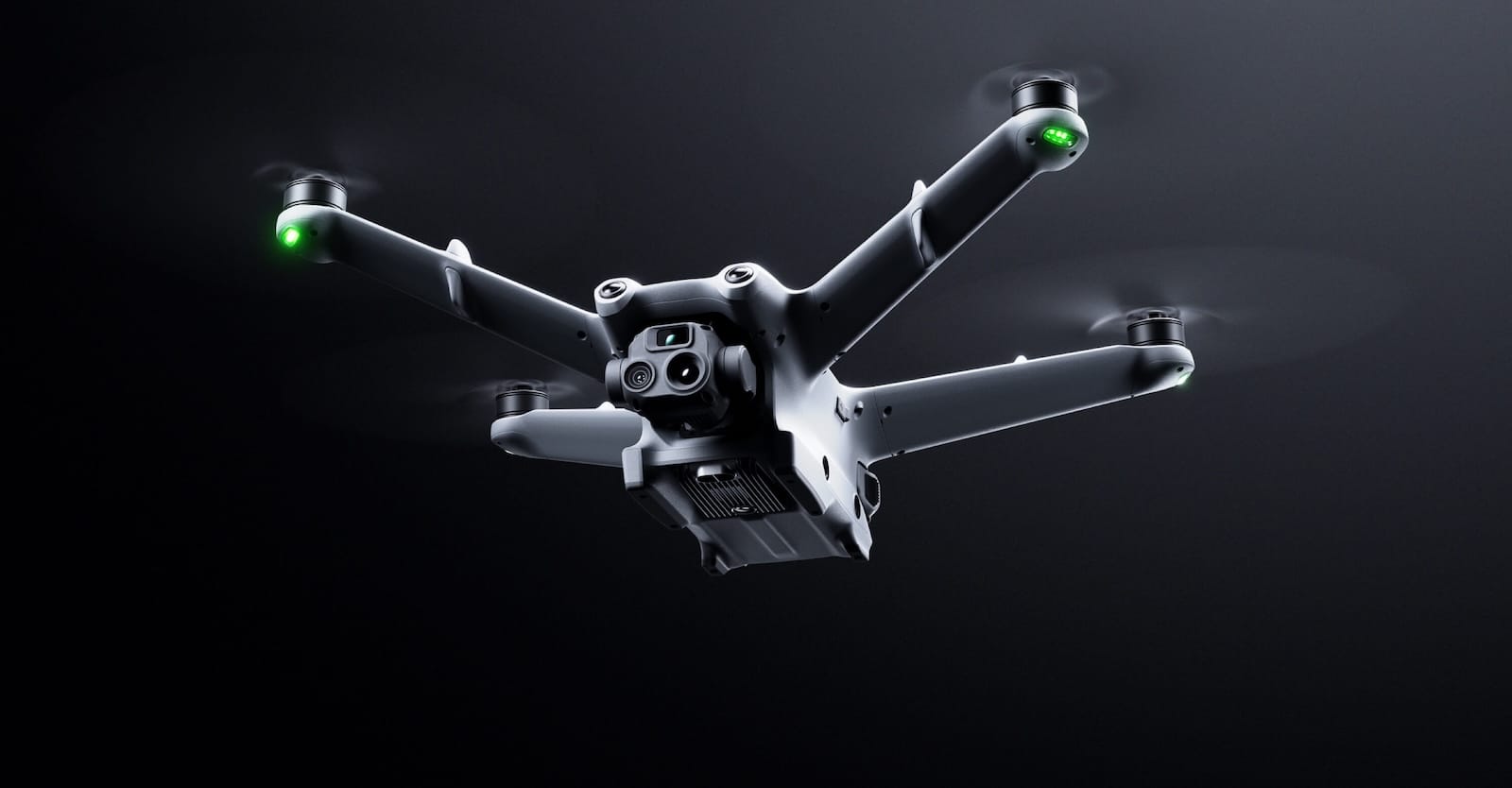 DJI Matrice 3D flying against a dark backdrop with its position lights lit.