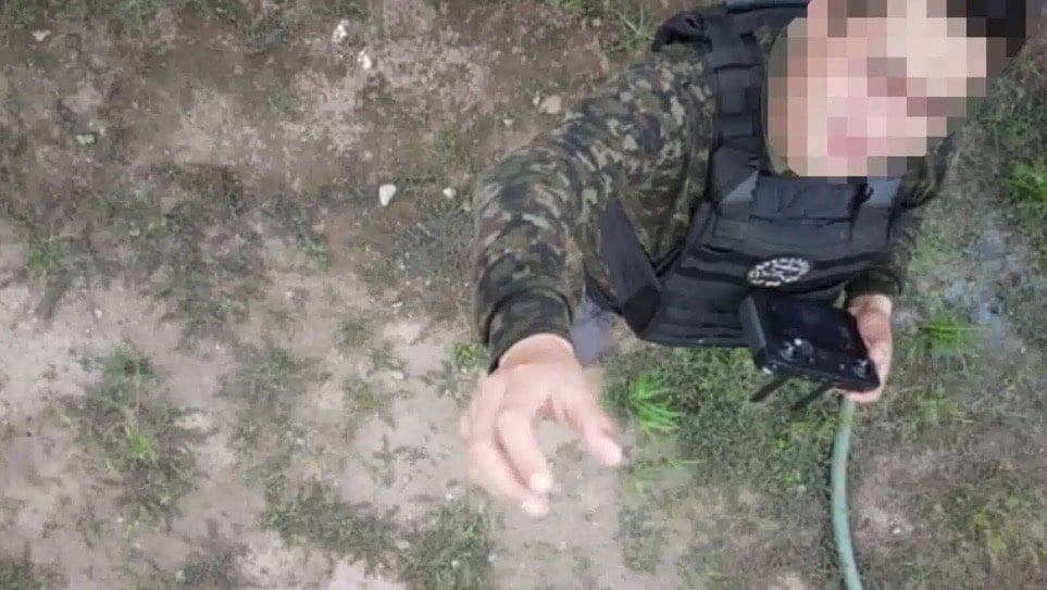 Drone view looking down at a masked man in camouflage reaching upward.