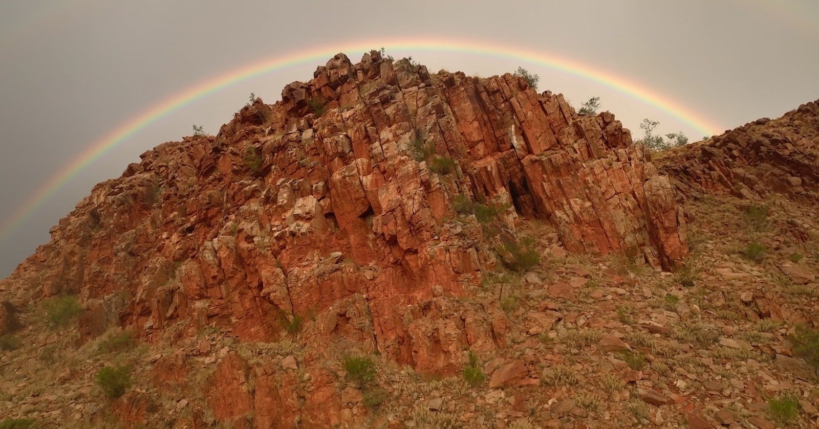 Aerial view of a red rock ridge under a full rainbow.