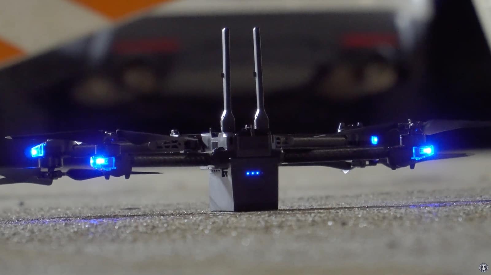 Close-up of a drone with blue LEDs and antennas resting on grass at dusk.