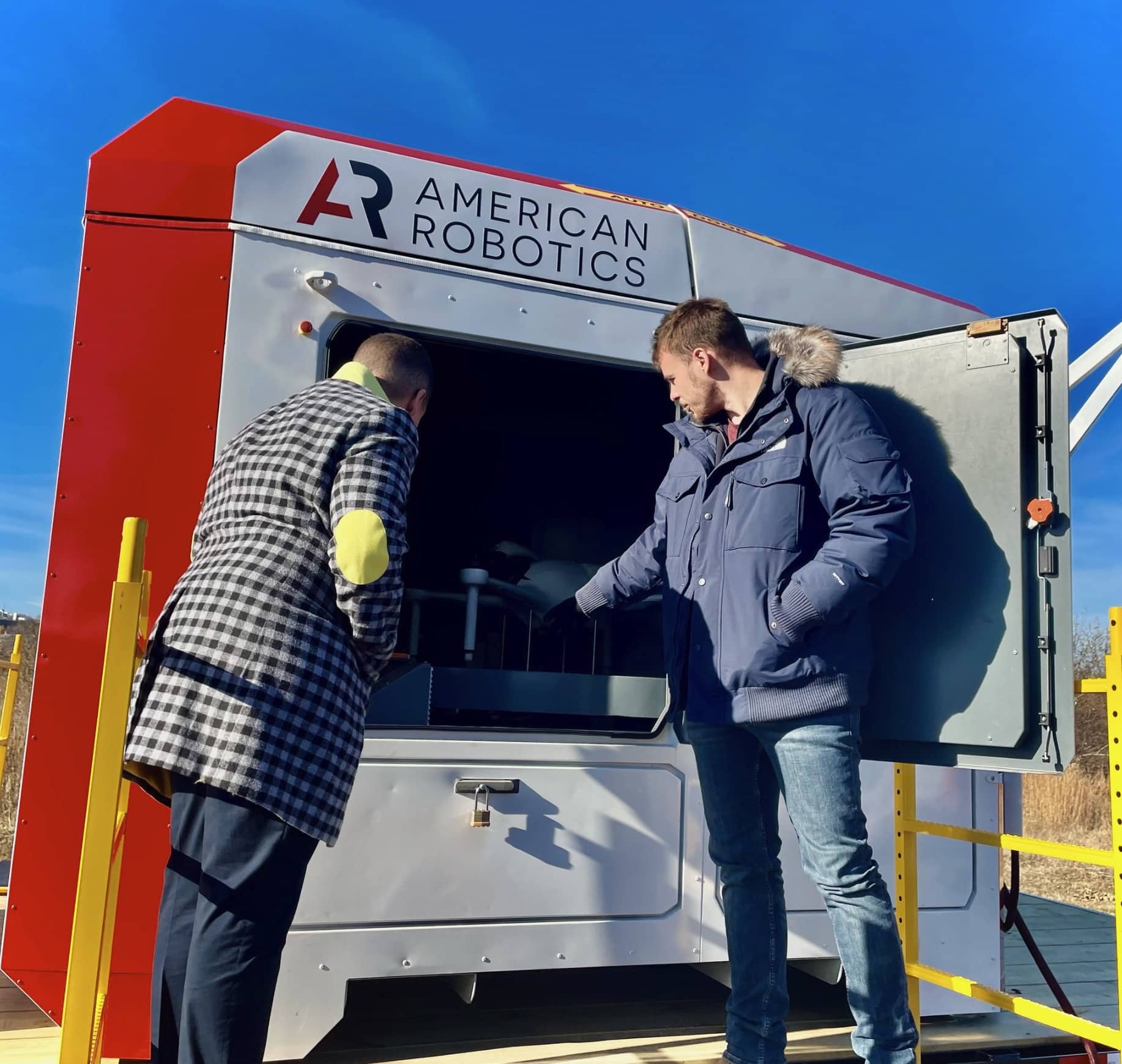 Two men inspect an American Robotics drone-in-a-box trailer in winter.