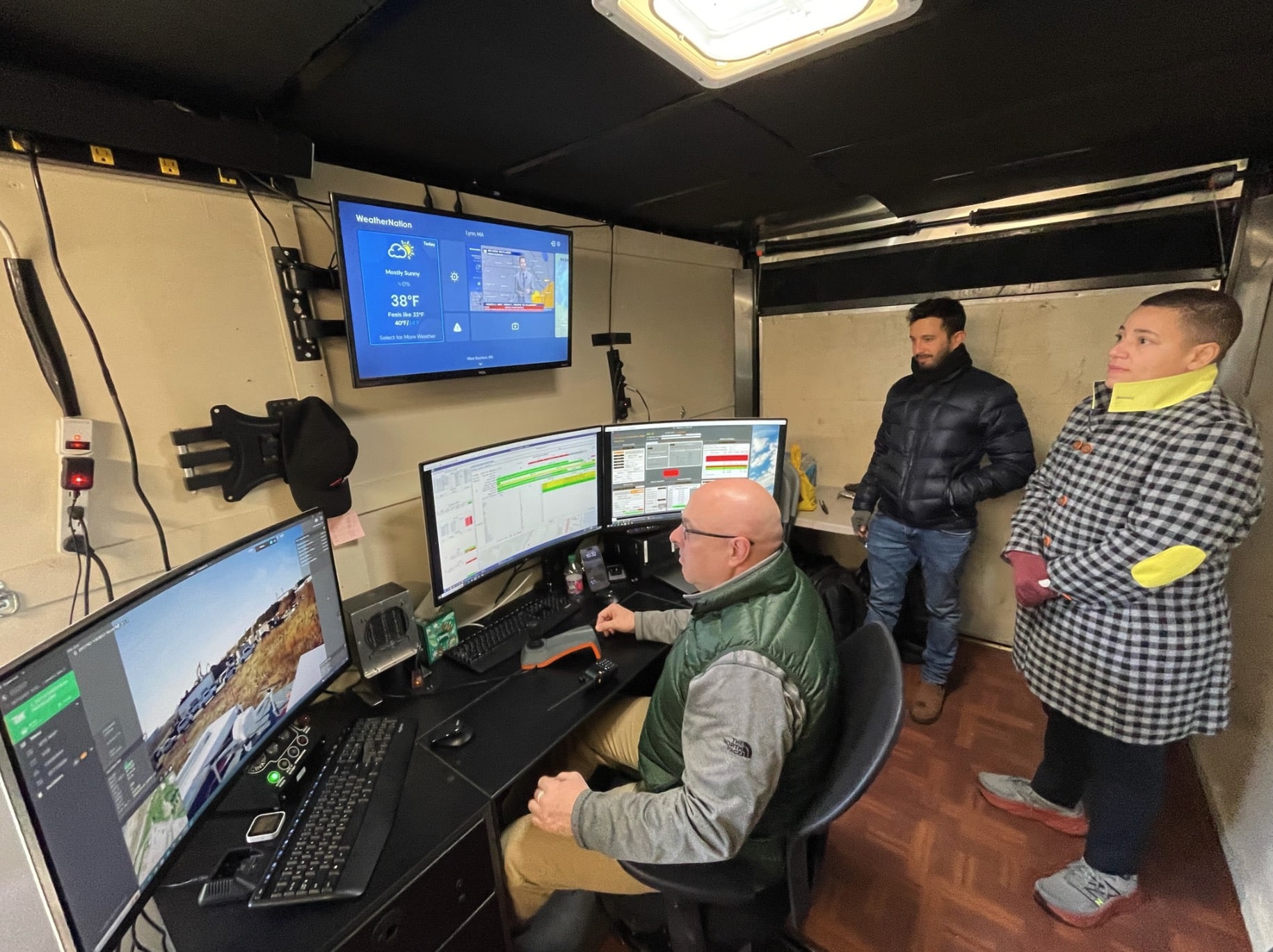 Operator at a multi-screen control desk while colleagues watch the drone feed.