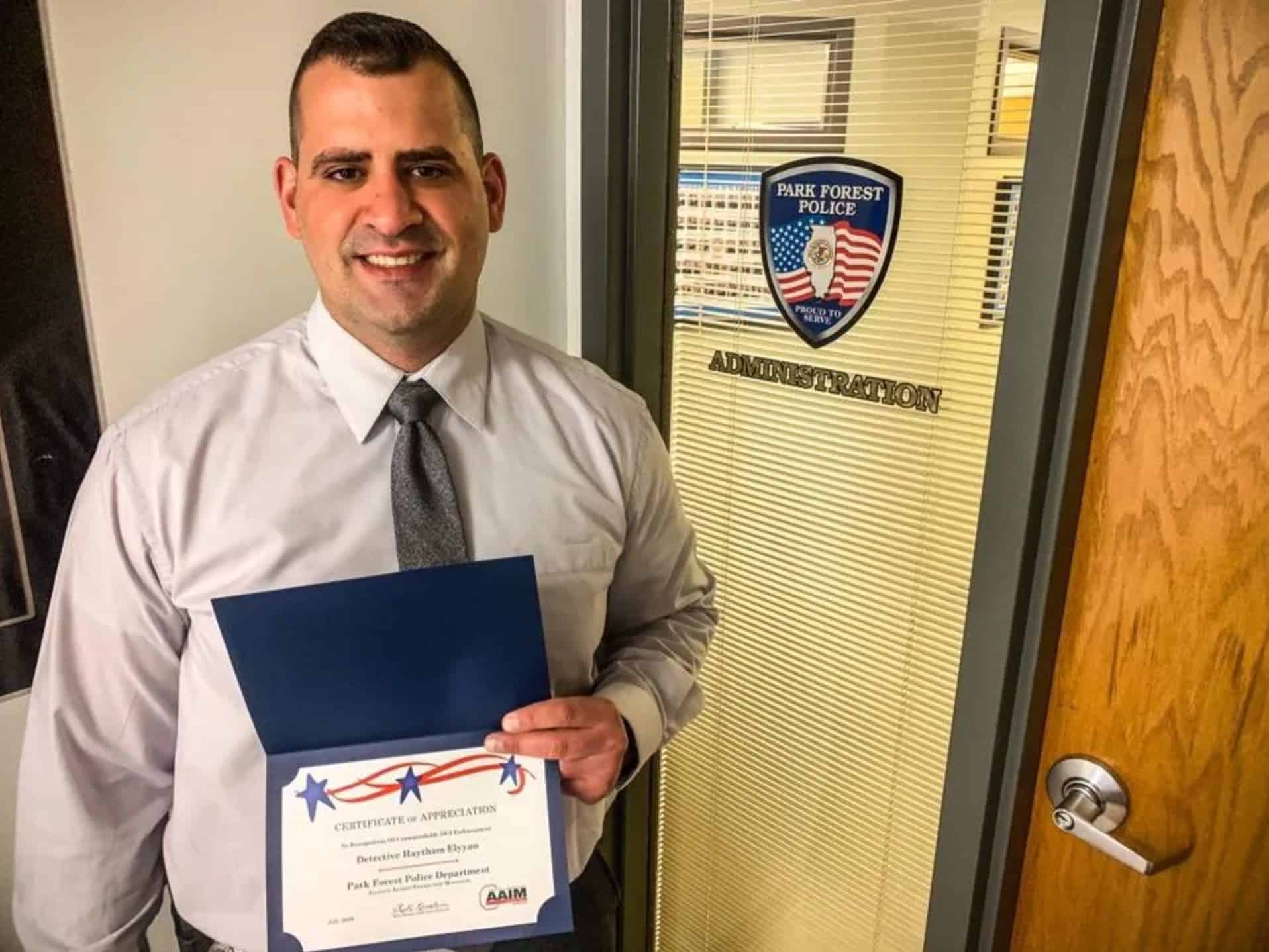 Park Forest police sergeant holding a certificate of appreciation outside the administration office.
