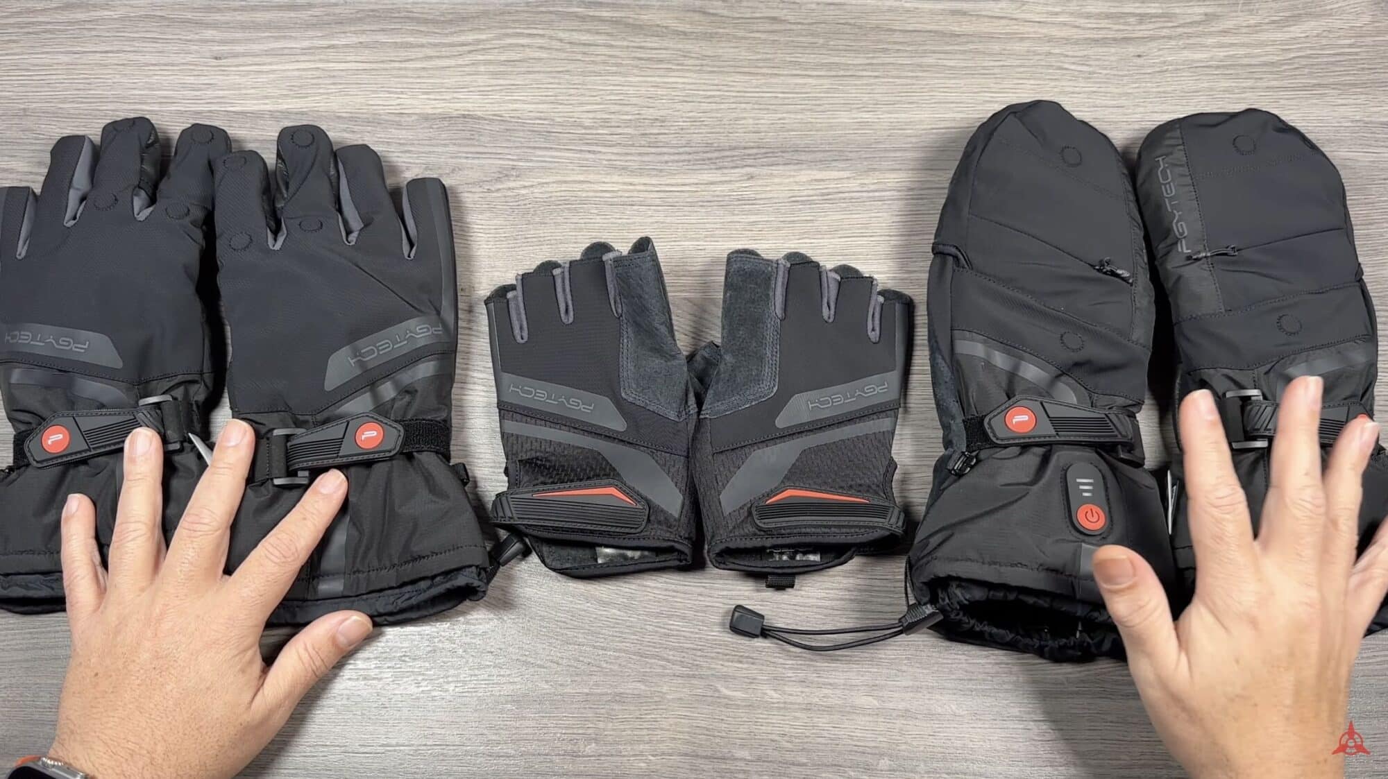 Three pairs of heated photography gloves laid out on a wooden floor.