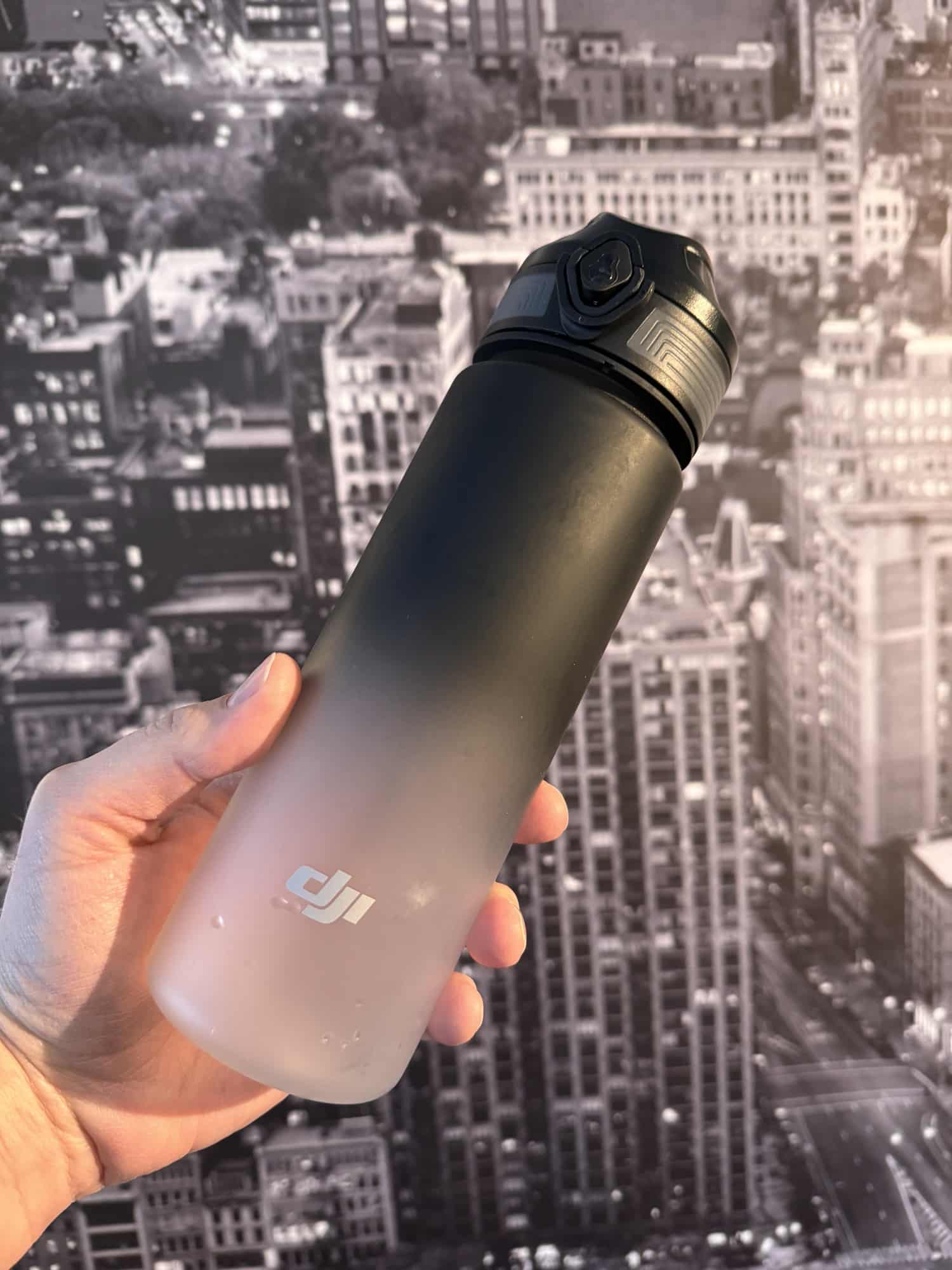 Hand holding a DJI branded sport water bottle against a city skyline backdrop.