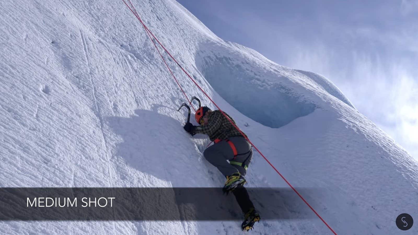 Medium shot following the climber partway up the iceberg.