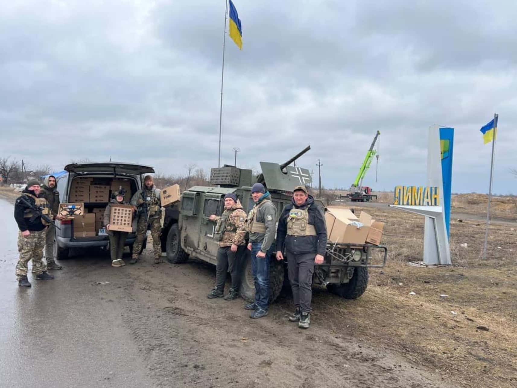 Volunteers unloading supply boxes beside a Humvee under a Ukrainian flag.