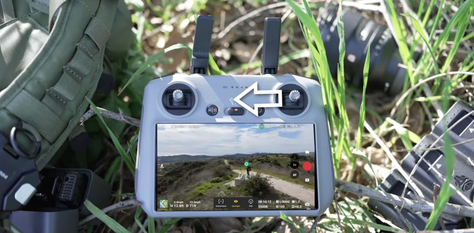 DJI RC Pro controller on grass beside a backpack, an arrow marking one button.