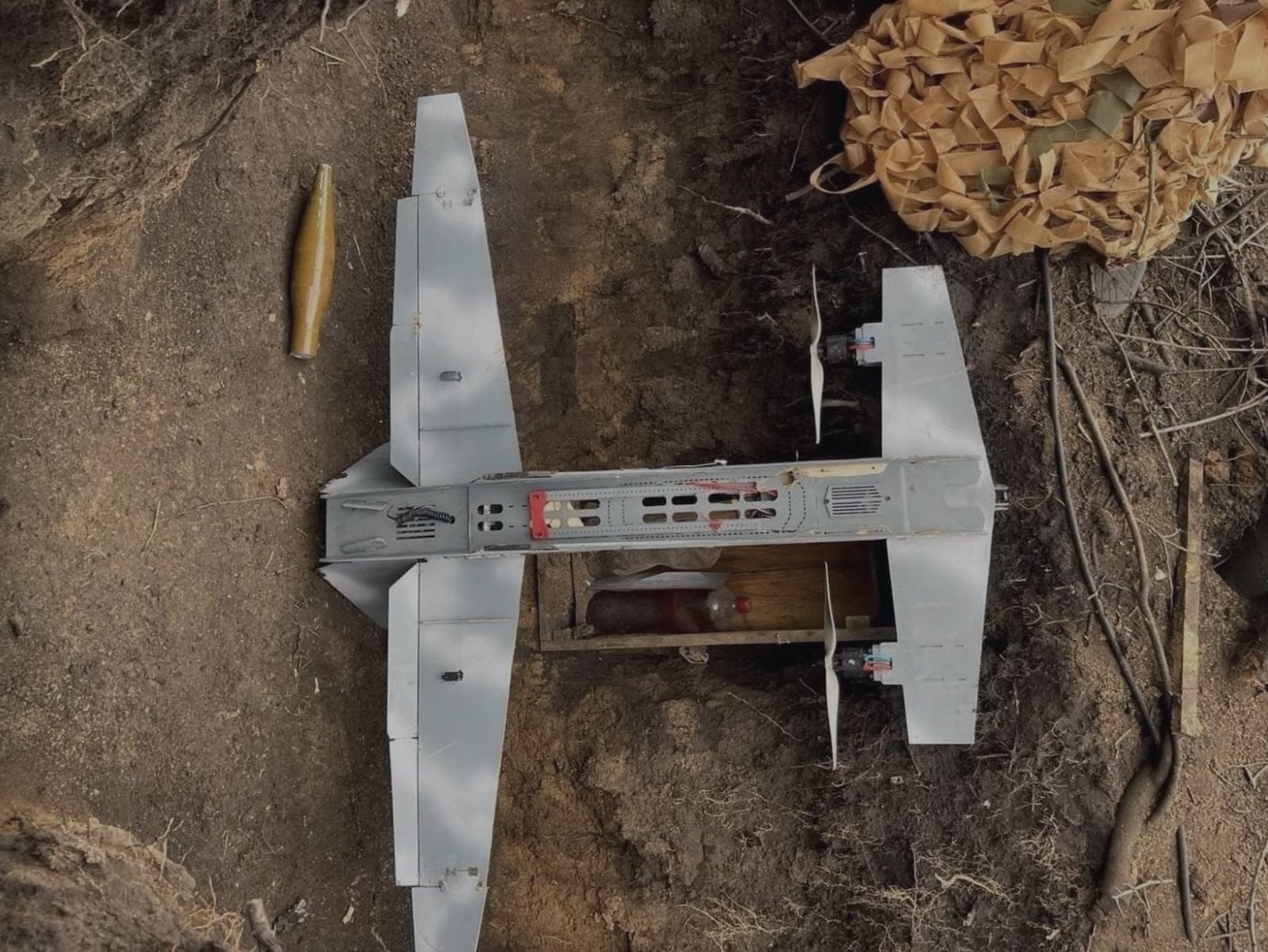 Captured Russian strike drone with white wings lying in a dirt trench.