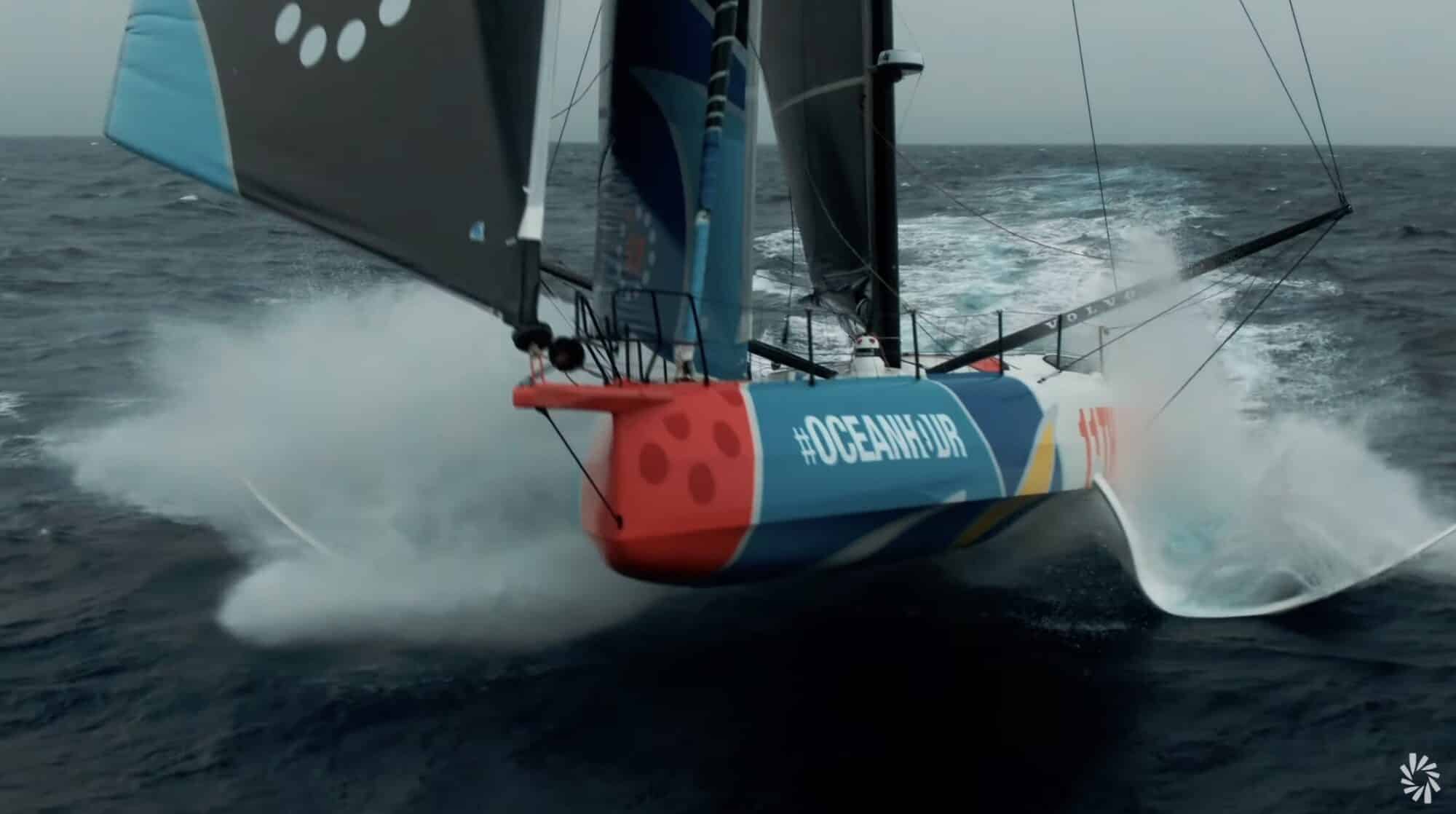 Ocean Race yacht foiling at speed through heavy spray seen from above.