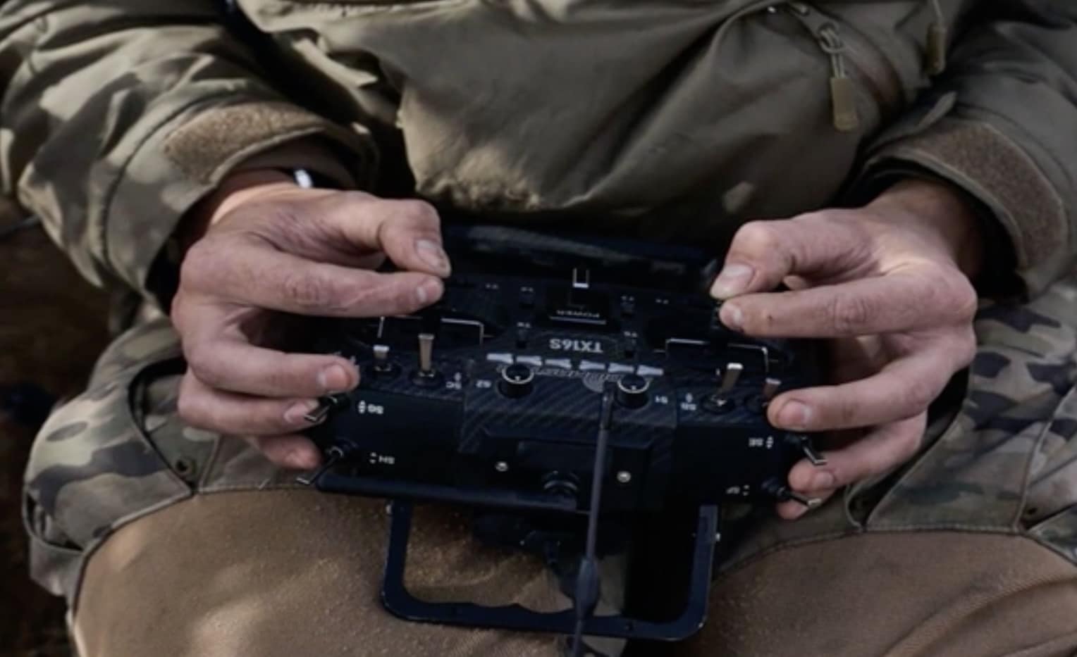 Soldier's hands on a multi-switch radio transmitter resting on camouflage clothing.