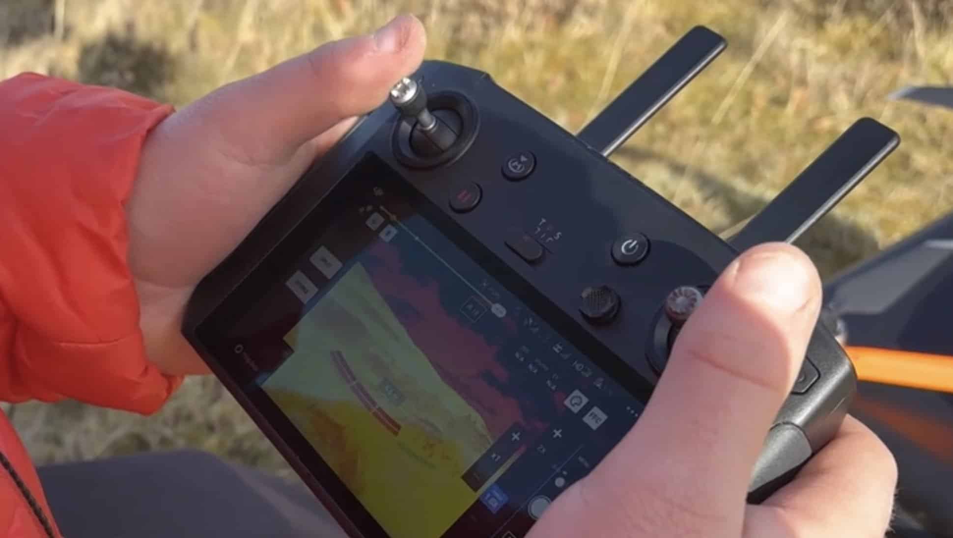 Rescue volunteer holds a drone controller showing a live thermal camera feed.