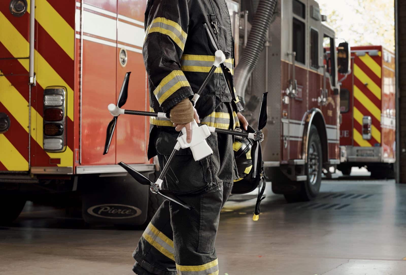 A firefighter in turnout gear carries a BRINC drone past a fire engine.
