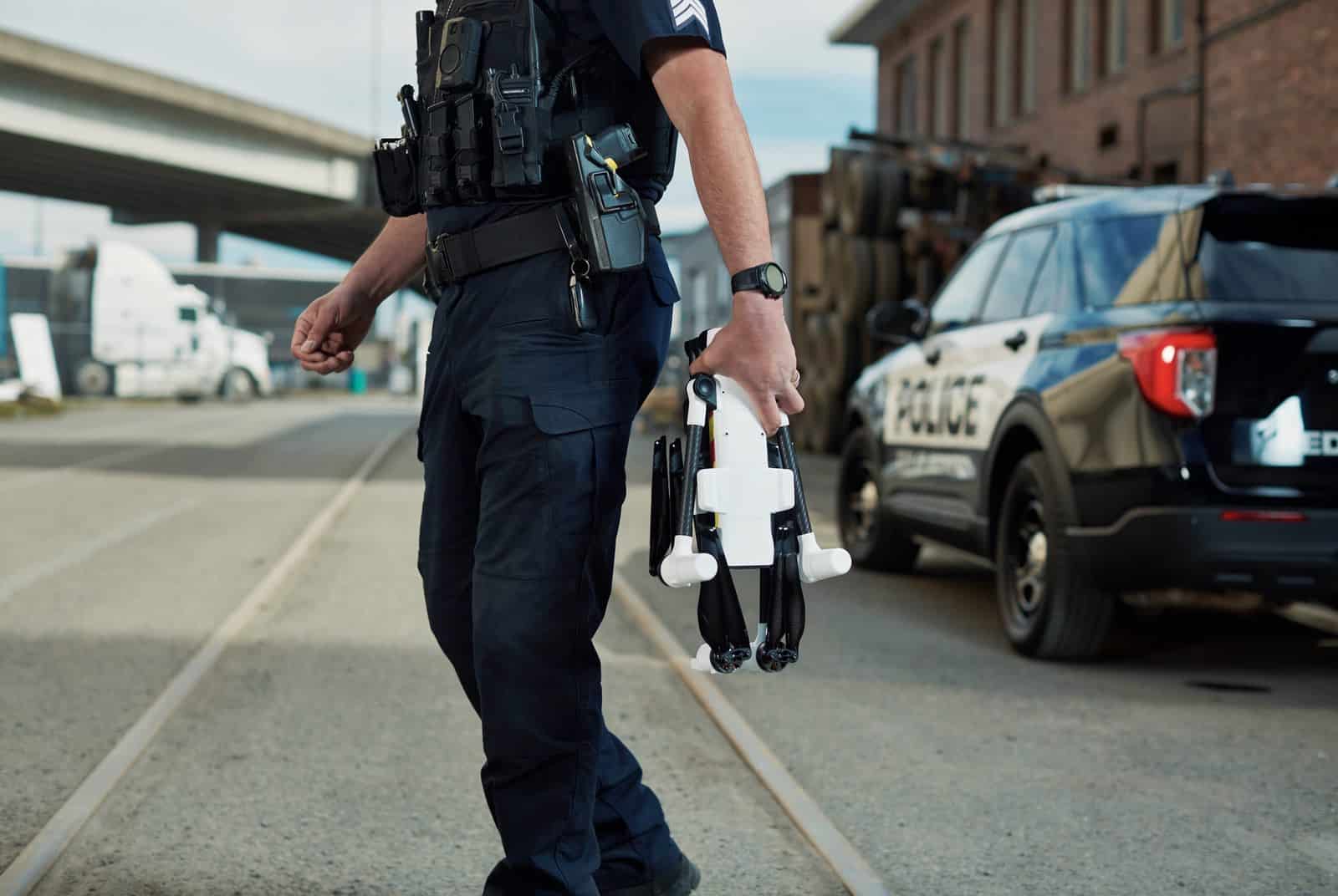 An officer carries a folded BRINC Responder drone alongside a police SUV.