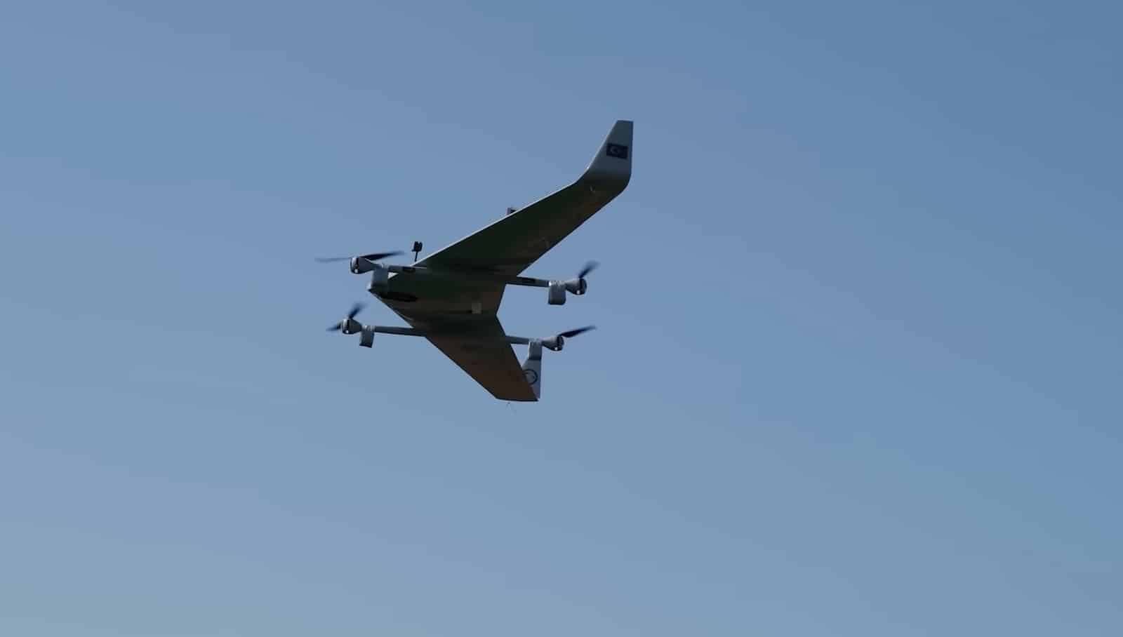 The tailless VTOL drone climbing steeply against clear blue sky, rotors turning.