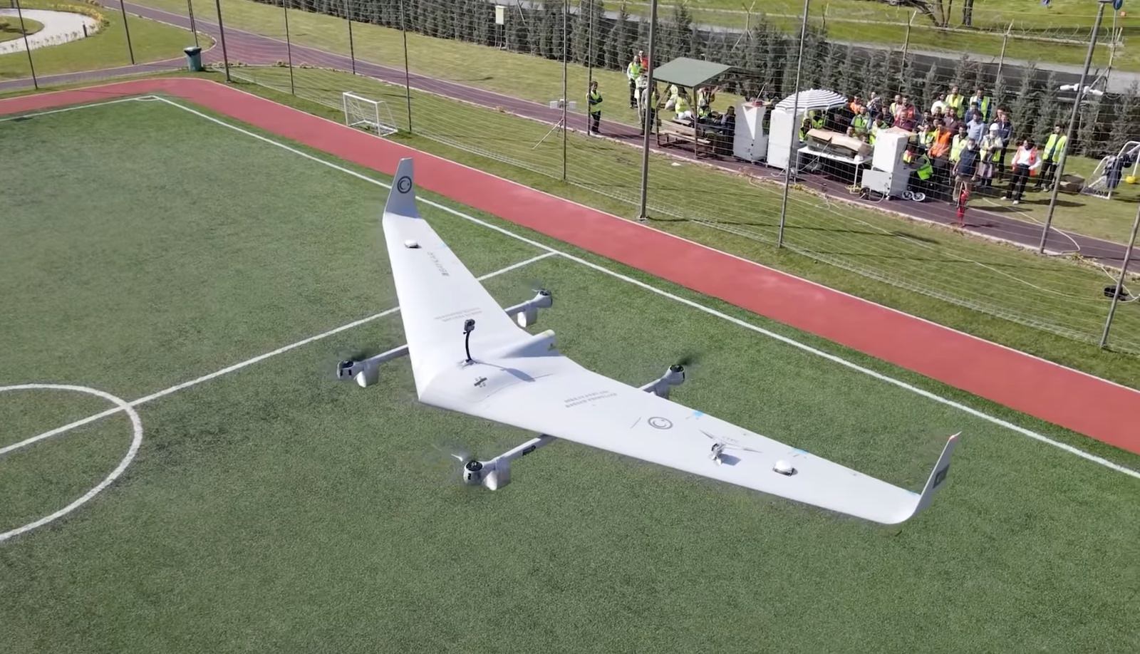 The drone resting on the pitch with spectators lining the running track behind.