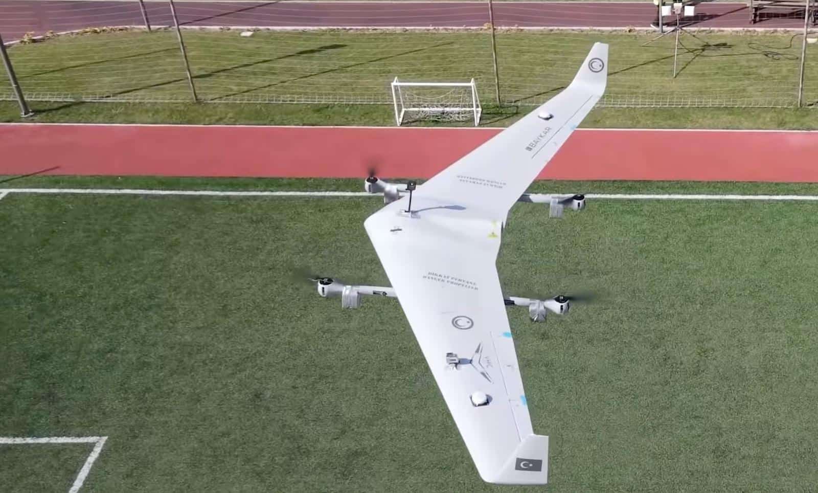 Overhead view of the drone on the grass with all four lift rotors spinning.