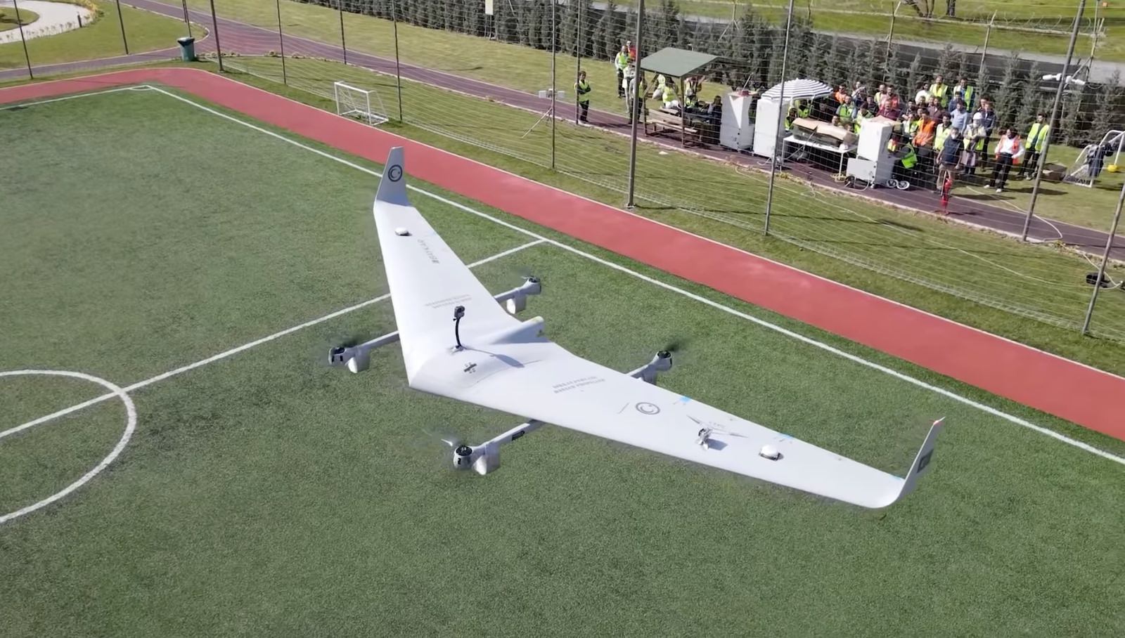 The parked flying wing on the pitch with officials gathered along the red track.