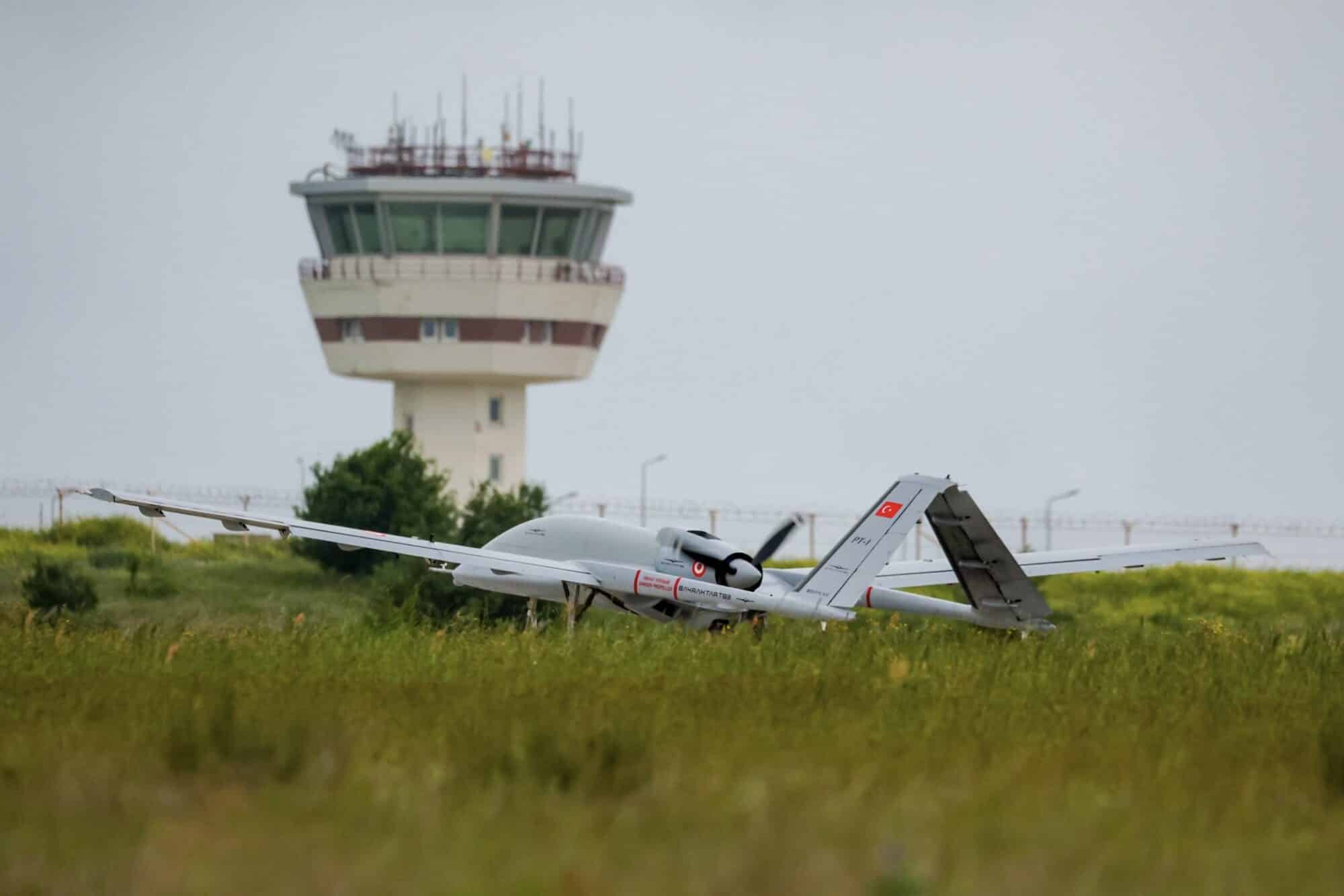 Bayraktar TB3 parked on grass in front of an airfield control tower.