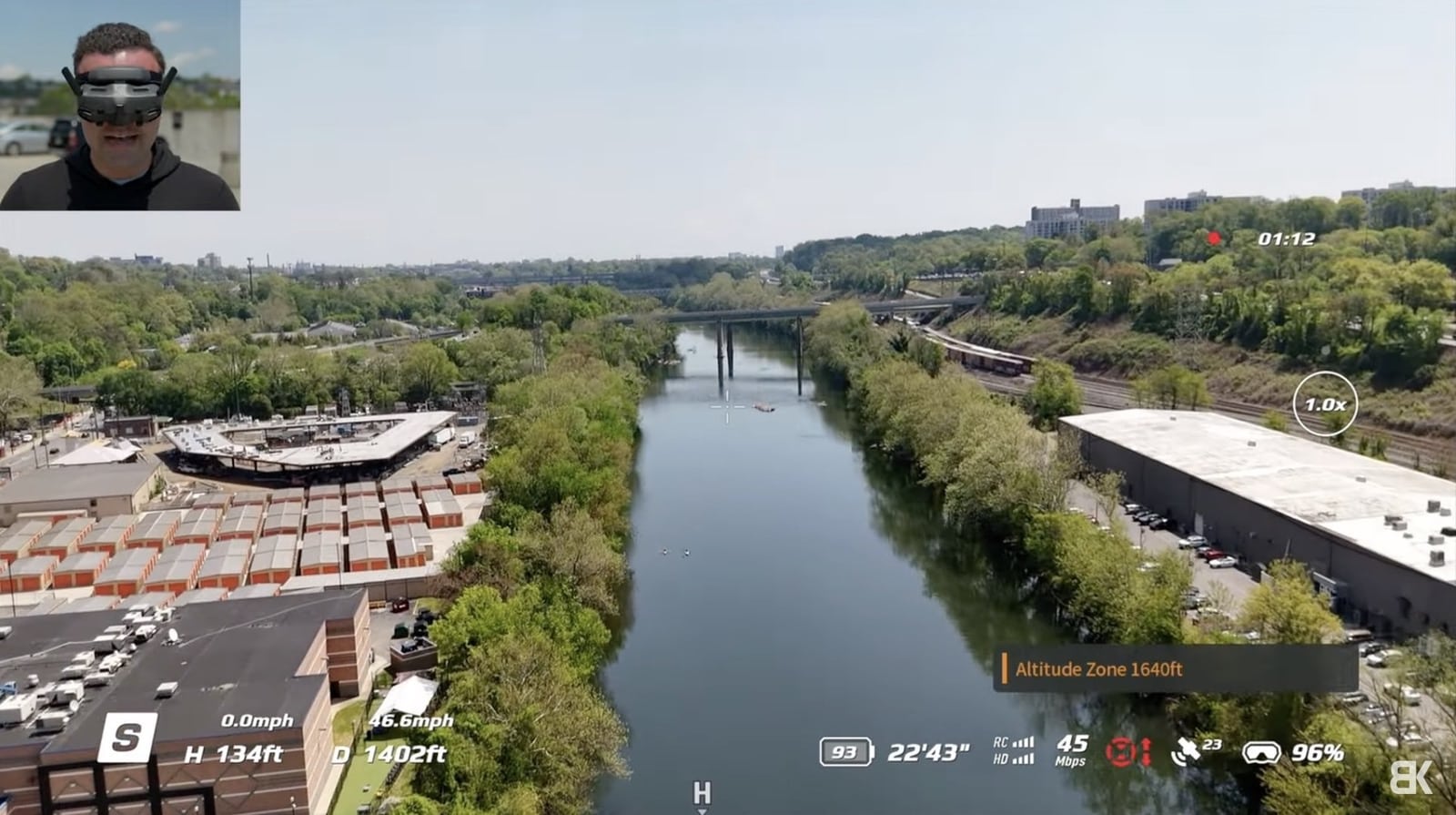 Goggles view of a river and rail bridge with telemetry and a pilot inset.