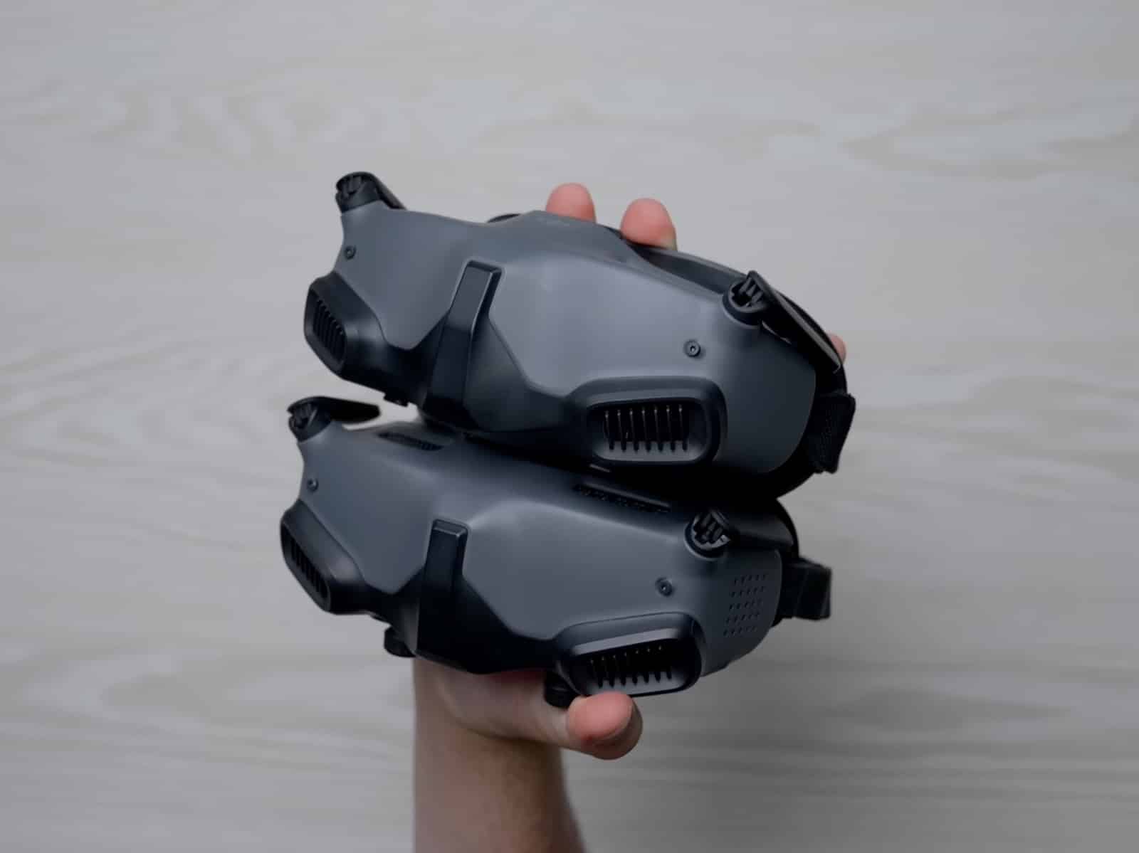Two DJI FPV goggle headsets stacked in one hand above a pale desk.