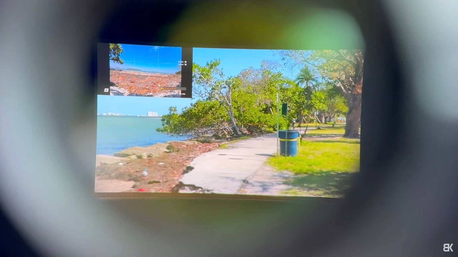 View through a goggle eyepiece showing a sunny waterfront park camera feed.